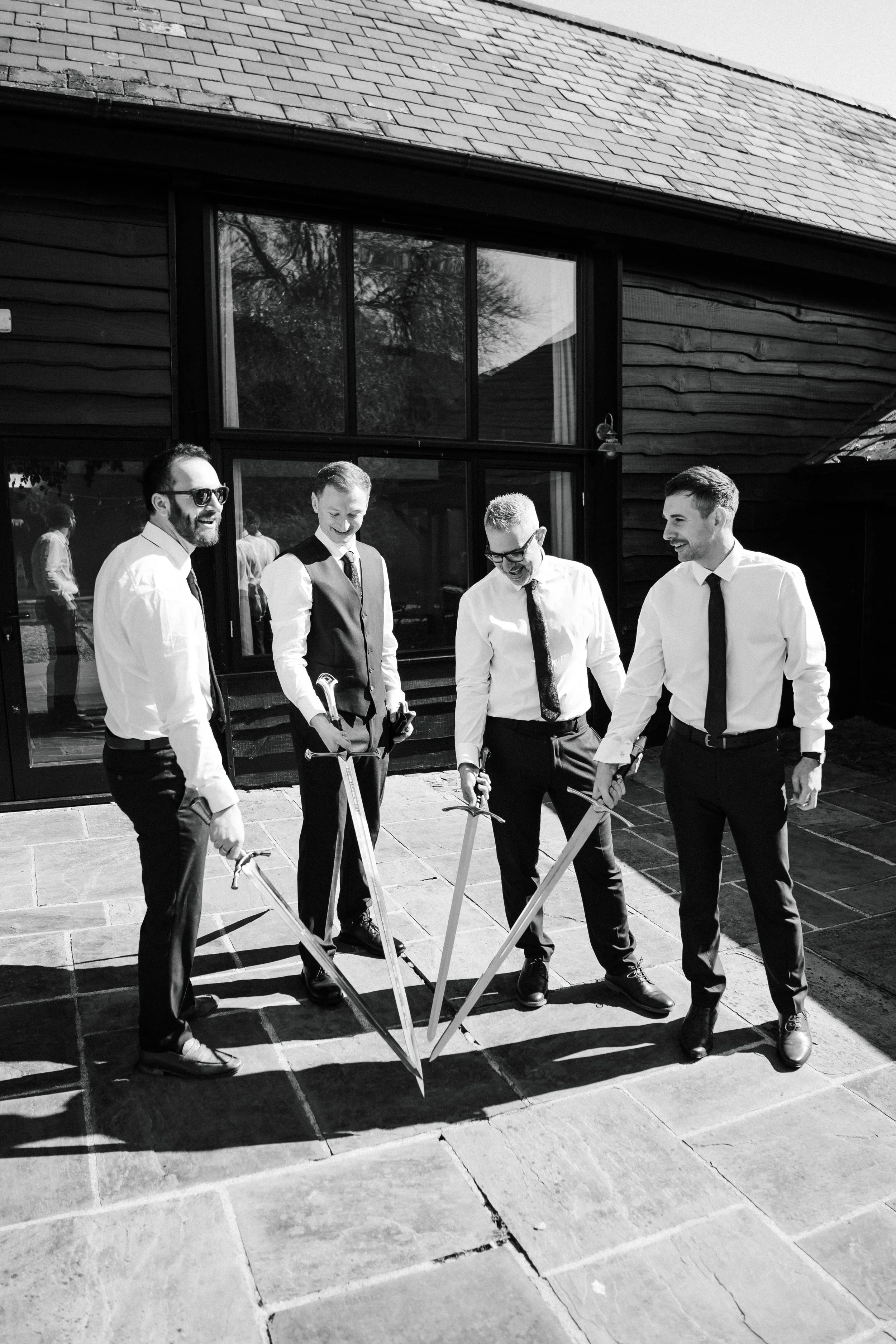 A group of five men dressed in formal attire, standing outdoors in front of a building, all smiling and holding shovels as if about to participate in a groundbreaking ceremony.