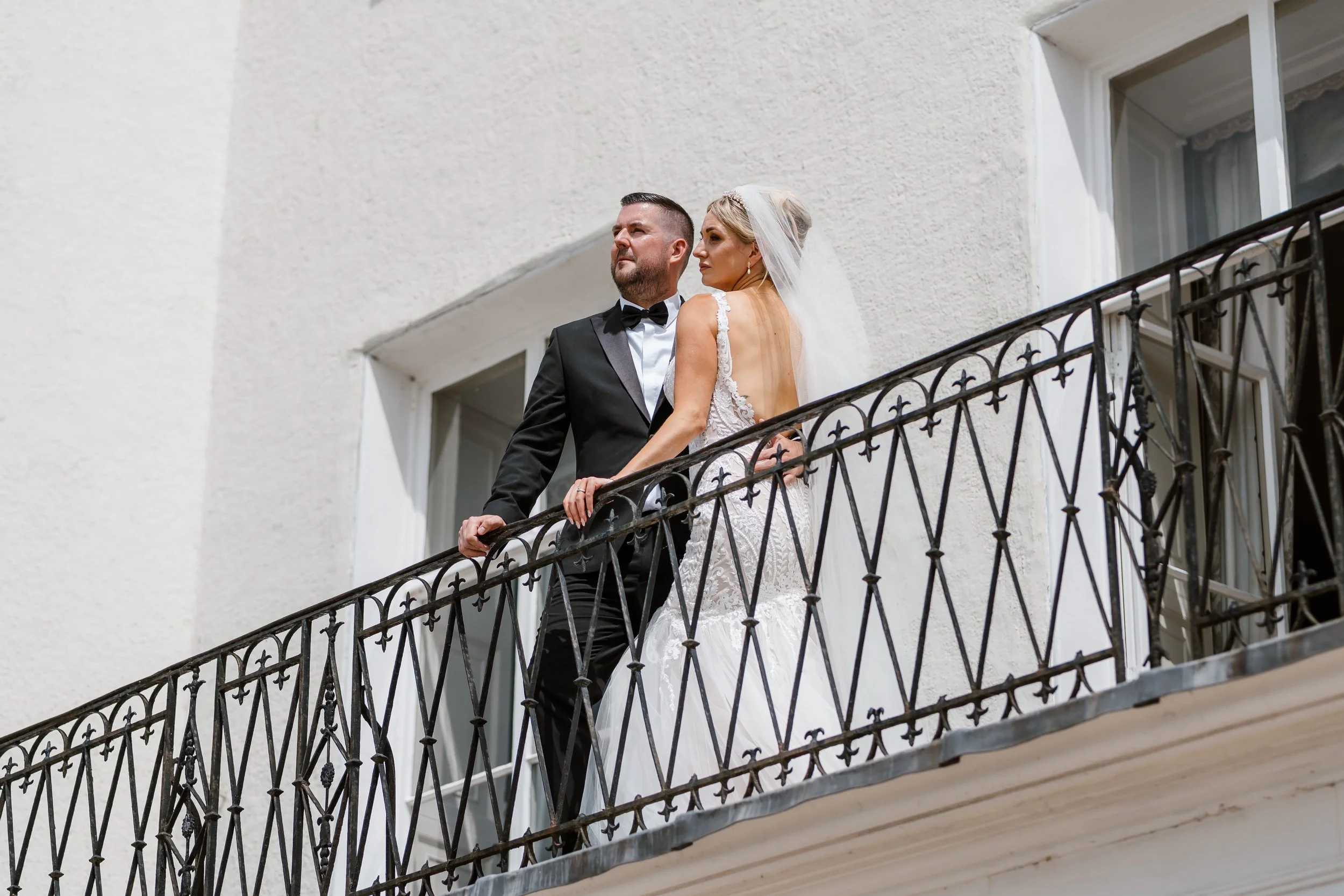A bride and groom standing on a balcony outside a white building.