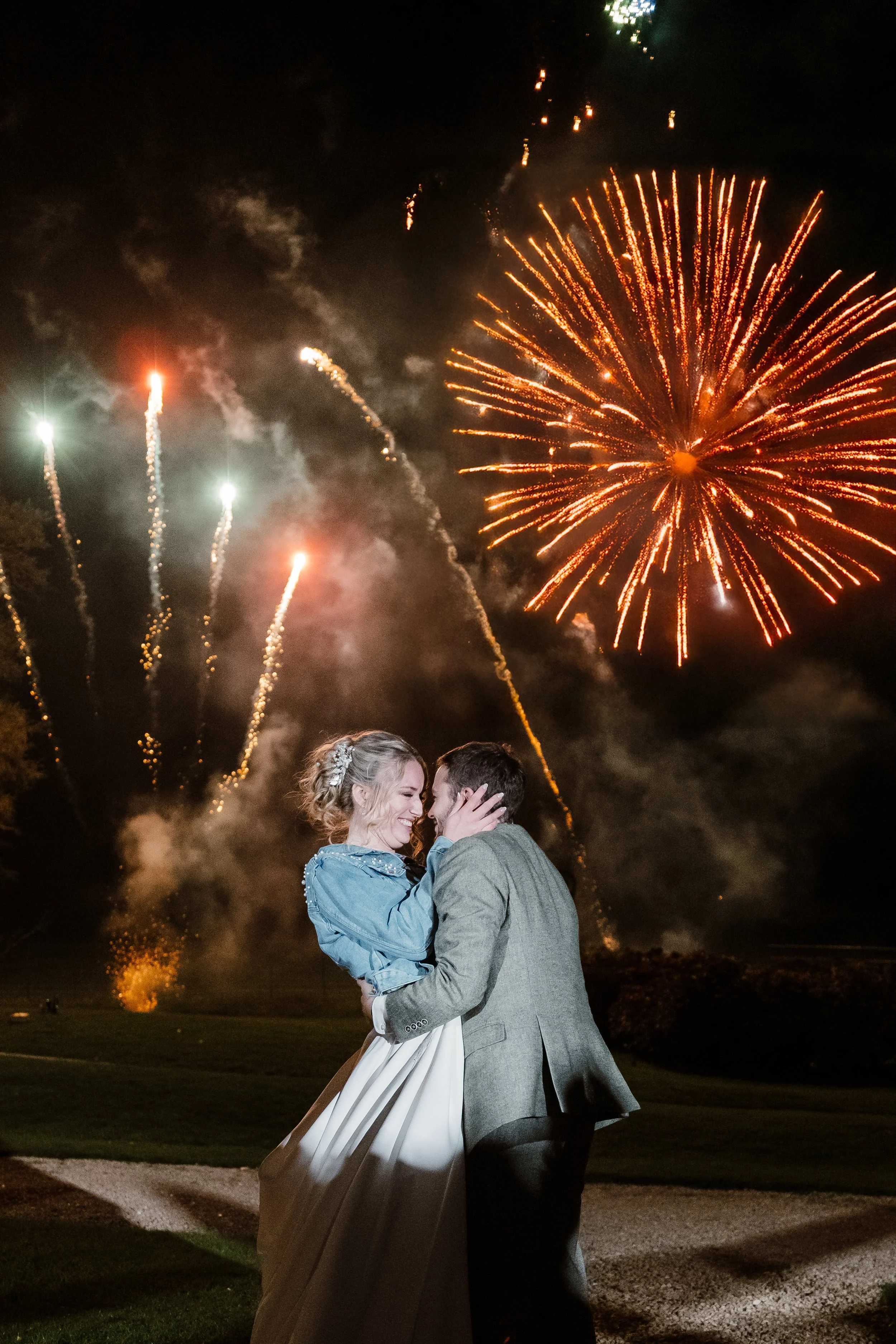 A couple dancing romantically outdoors at night with fireworks in the sky.