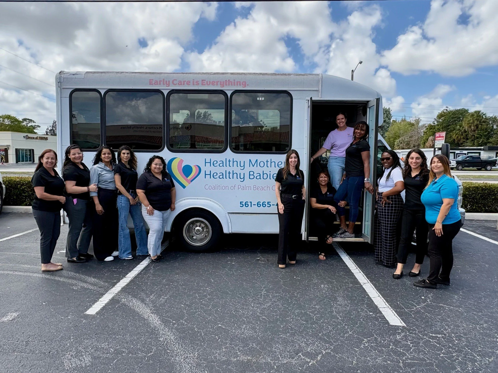 Healthy Mothers, Healthy Babies staff standing beside the Basics4Babies Emergency Pantry for Infants mobile bus, which provides diapers, infant formula, baby food, and other essential supplies to families in Palm Beach County.