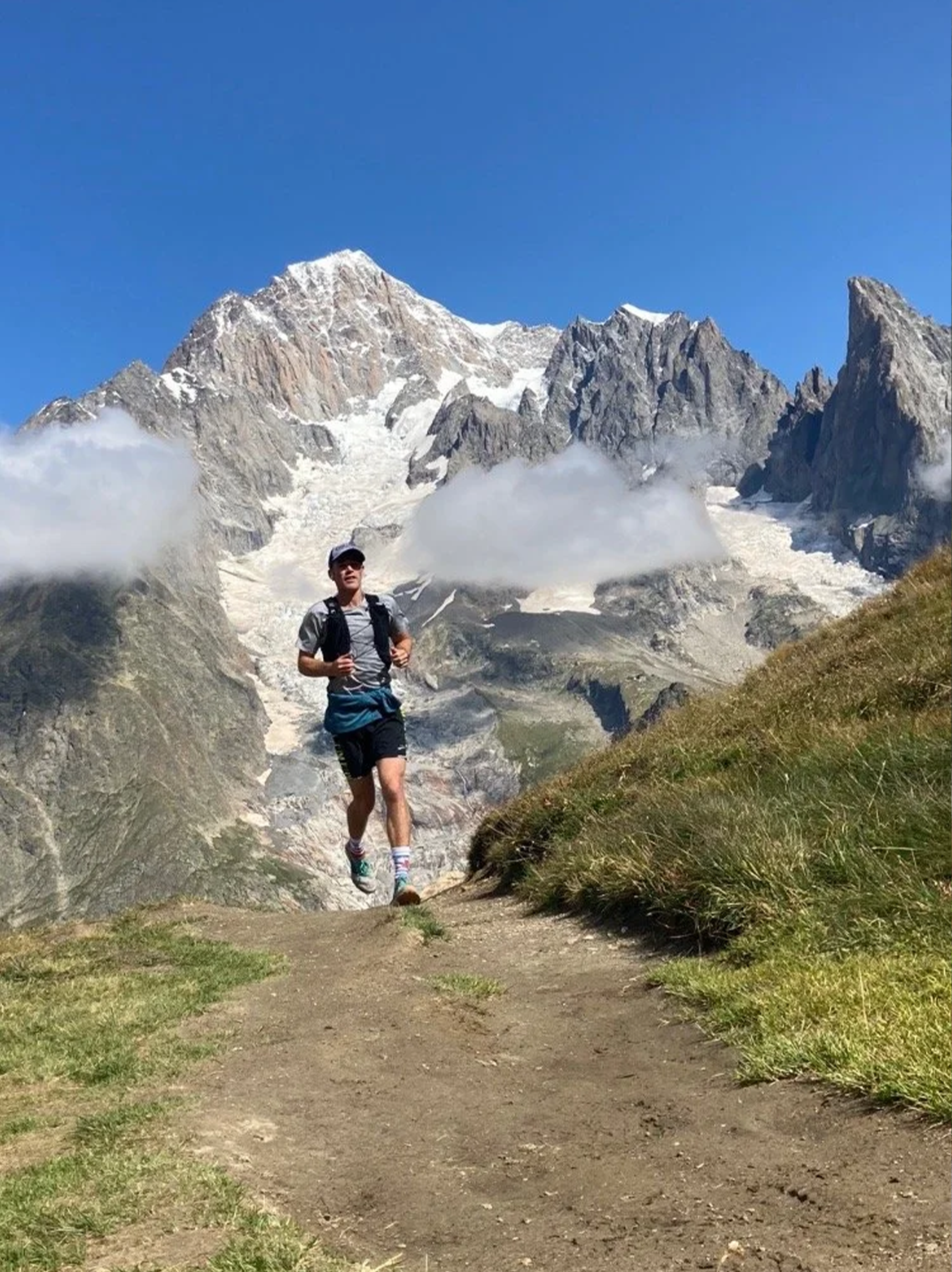 A person hiking in a mountainous area with snow-capped peaks, rocky cliffs, and a clear blue sky in the background in Portland Oregon.