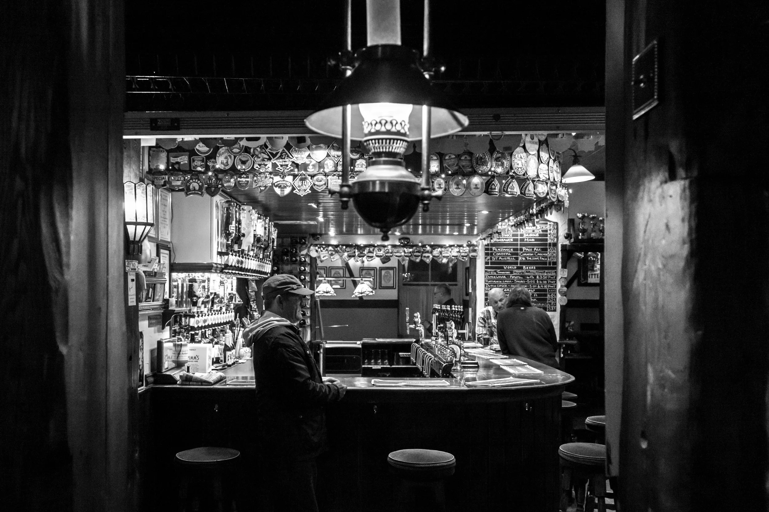 Patrons stand at the bar, beneath lights, bottles, and assorted pump clips. Photograph by Morgan Webb