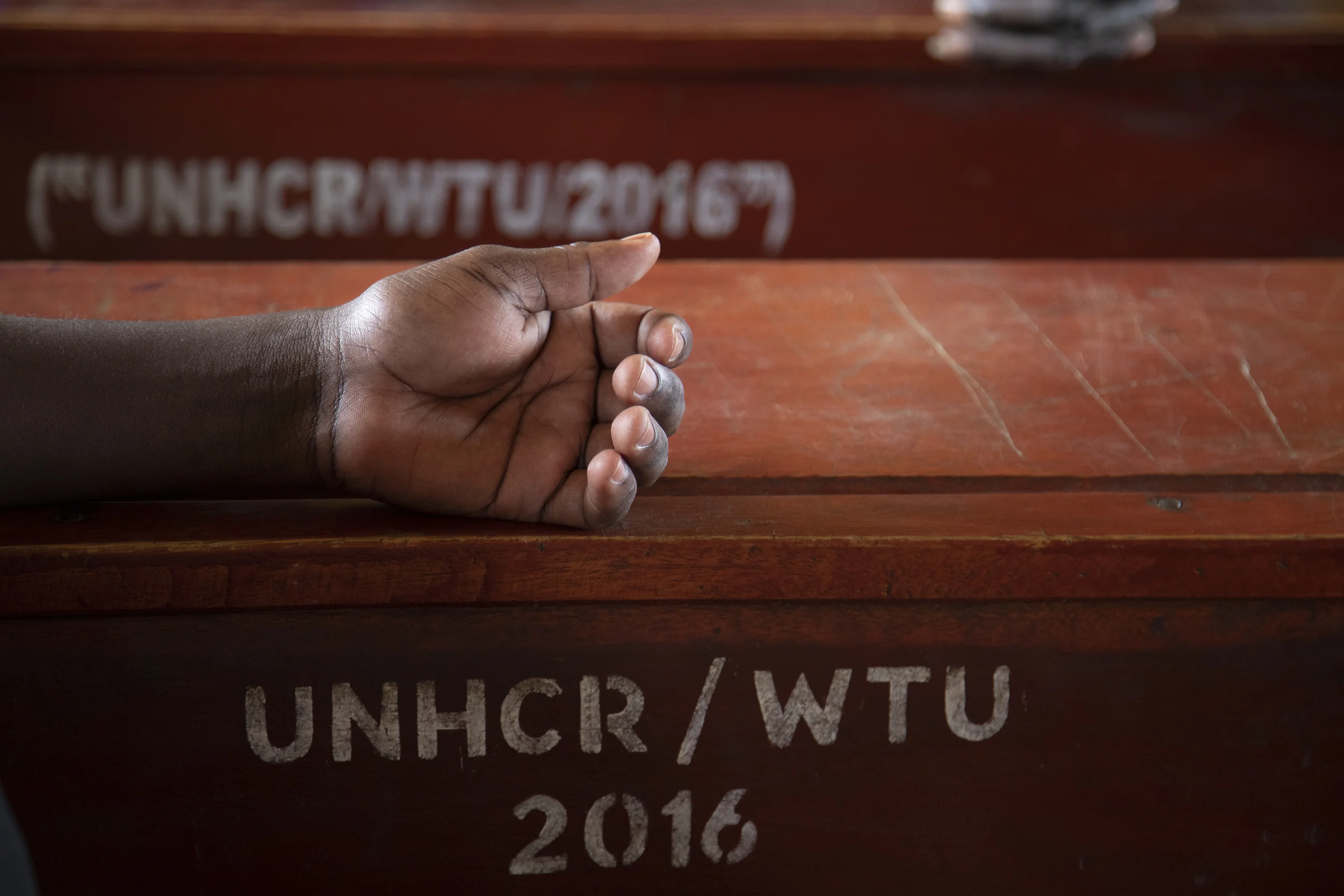 A child’s hand rests on a school desk provided by the UNHCR.