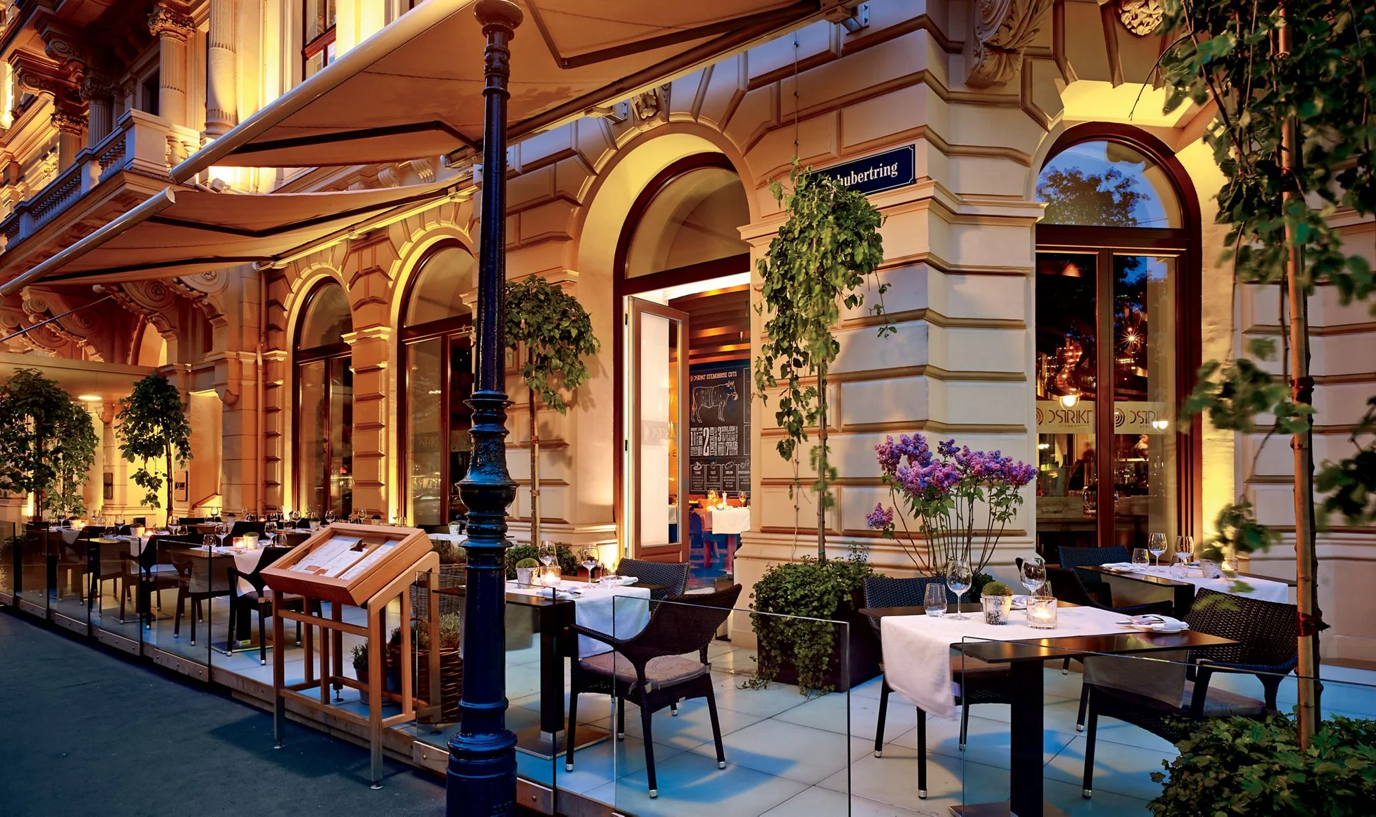 Patio seating wraps around the corner of the building and features potted plants and tables at the Ritz-Carlton in Vienna, Austria.
