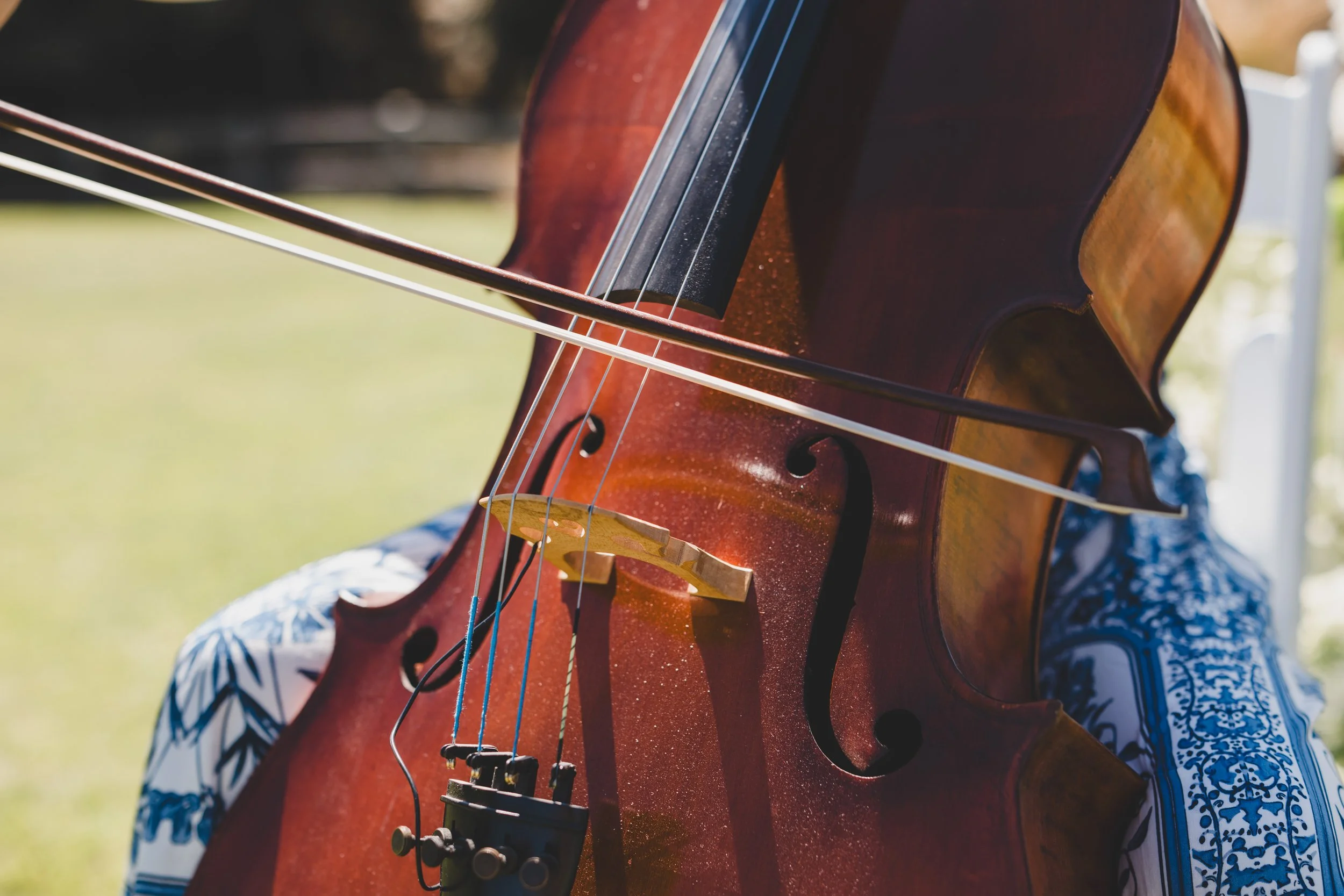 A woman playing a cello indoors, with music sheets on stands in front of her and flowers in the foreground.