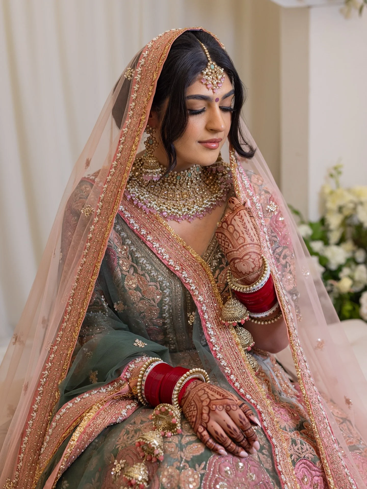 2/3 - Gracefully veiled, Sonya radiates elegance on her wedding day in a stunning sage green and blush lehenga, adorned with intricate embroidery and timeless jewels. Her serene smile, detailed mehndi, and regal poise capture the essence of a truly b