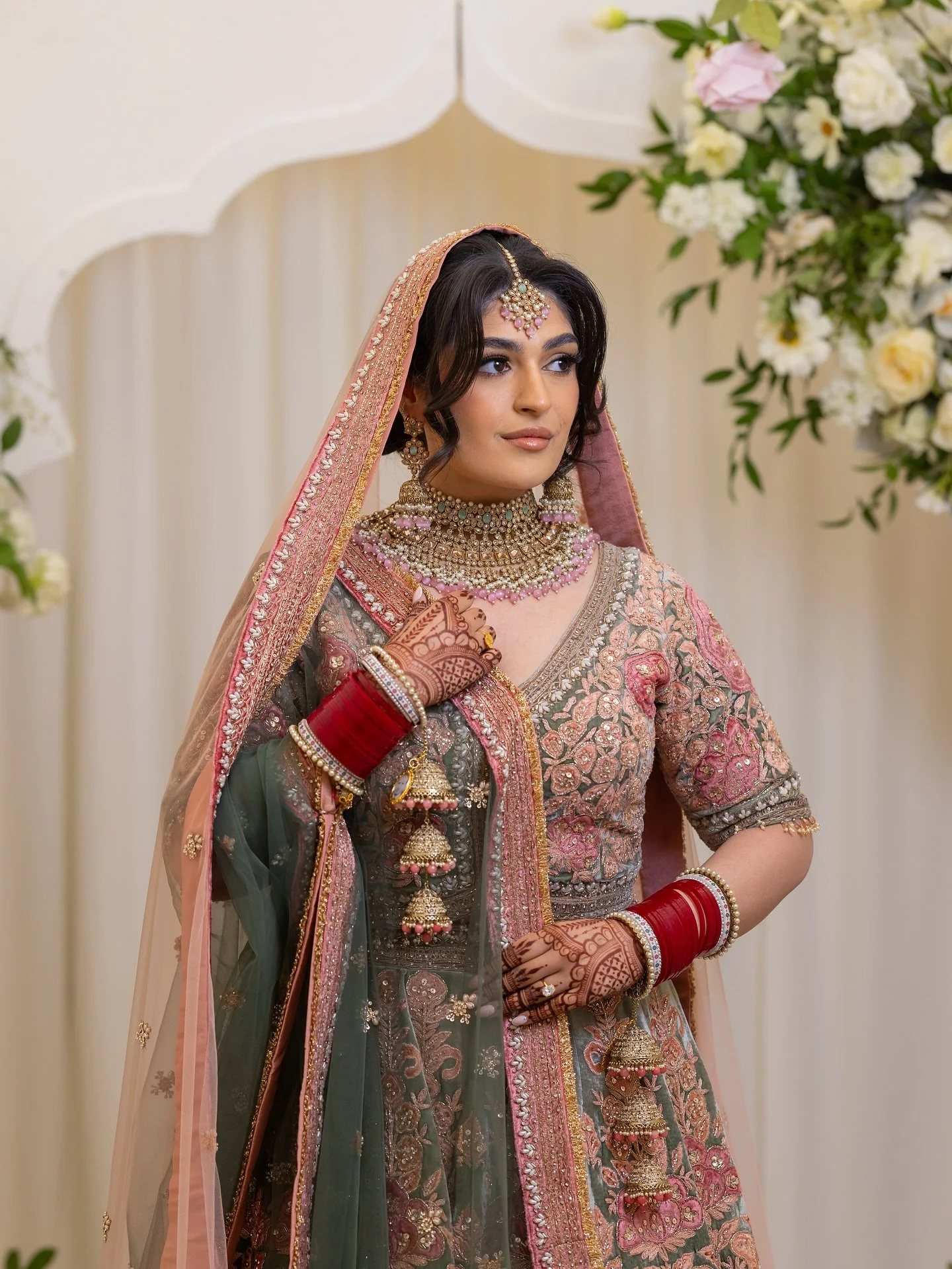 1/3 - Sonya looks absolutely radiant on her wedding day, adorned in an exquisite pastel lehenga intricately detailed with floral embroidery in soft shades of blush pink, sage green, and shimmering gold. The elegance of her bridal look is enhanced by 