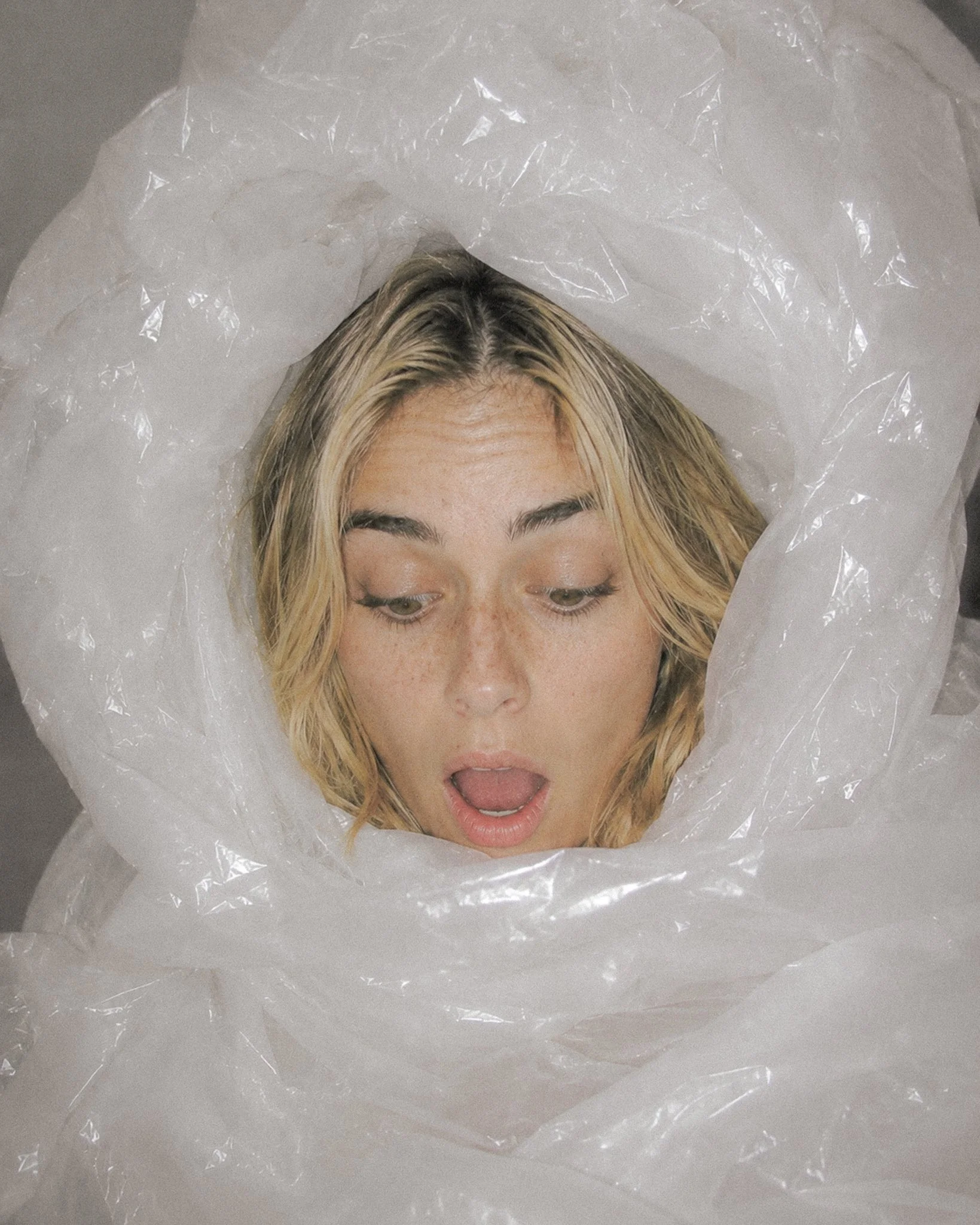 Femme enveloppée dans un sac plastique transparent, yeux mi-clos, expression d'épuisement – critique du greenwashing et du cuir vegan synthétique dans la mode – Blog Les Mains d'ici