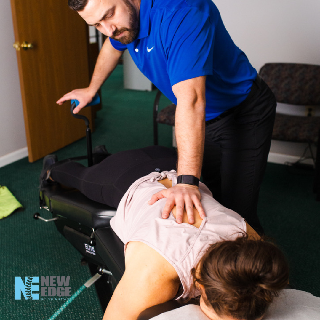A chiropractor performing a spinal adjustment on a woman lying face down on a chiropractic table in an office setting.