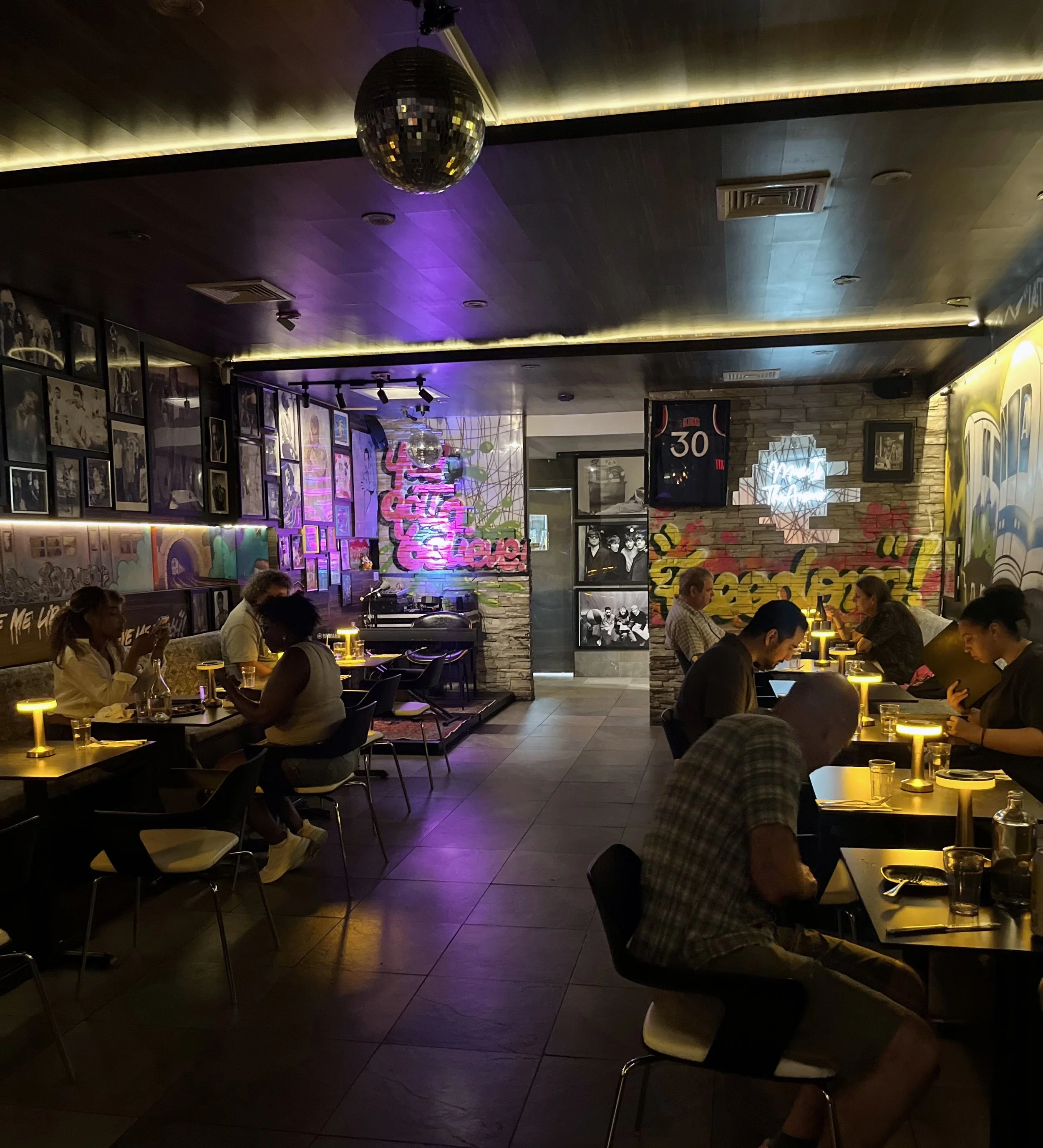 Guests dining at Urban Vegan Kitchen in Chelsea, NYC, surrounded by murals, art and warm evening lighting.