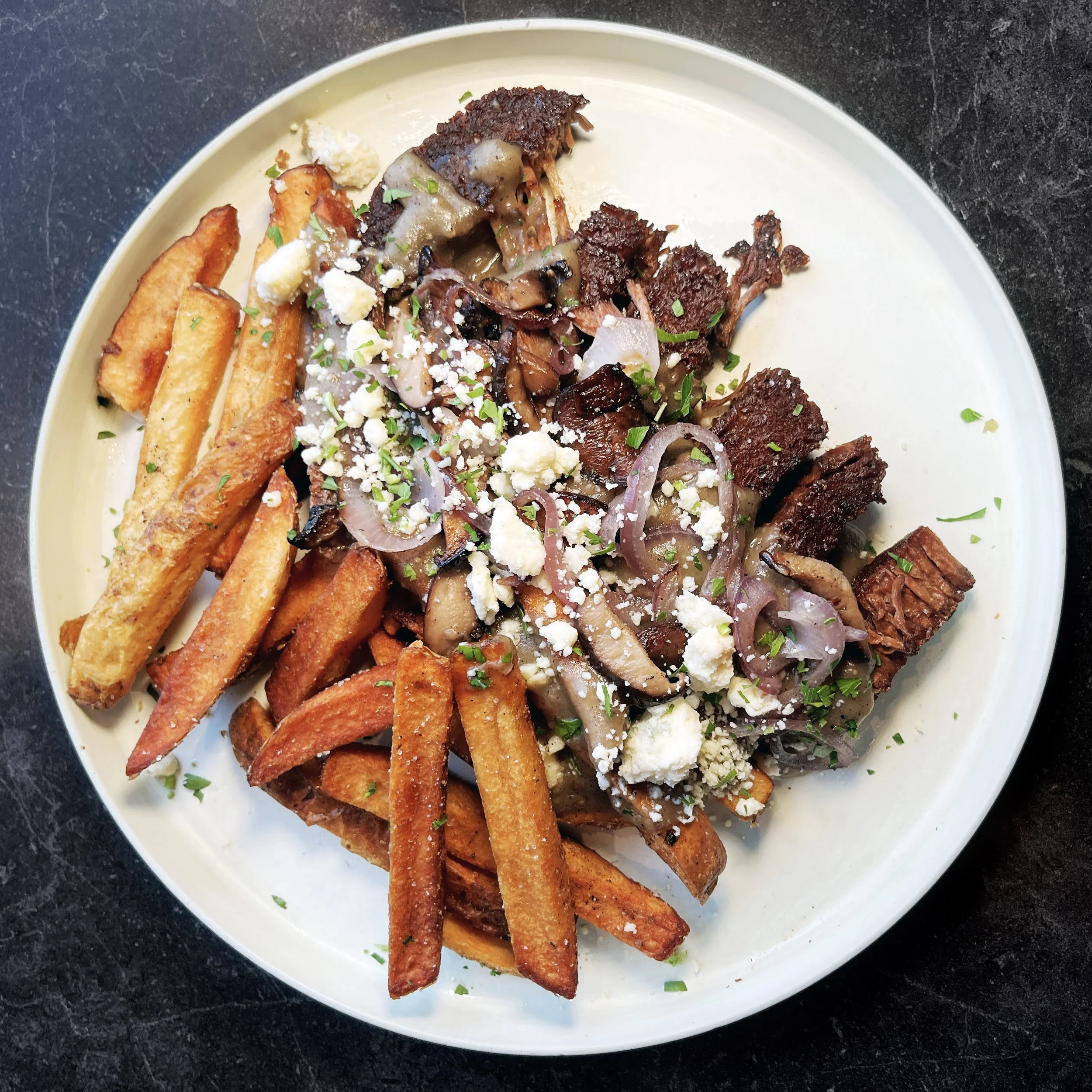 Vegan steak frites with Chunk steak, thick-cut fries, housemade gravy, grilled mushrooms and onions, vegan bleu cheese, and parsley at Urban Vegan Kitchen in Chelsea, NYC.