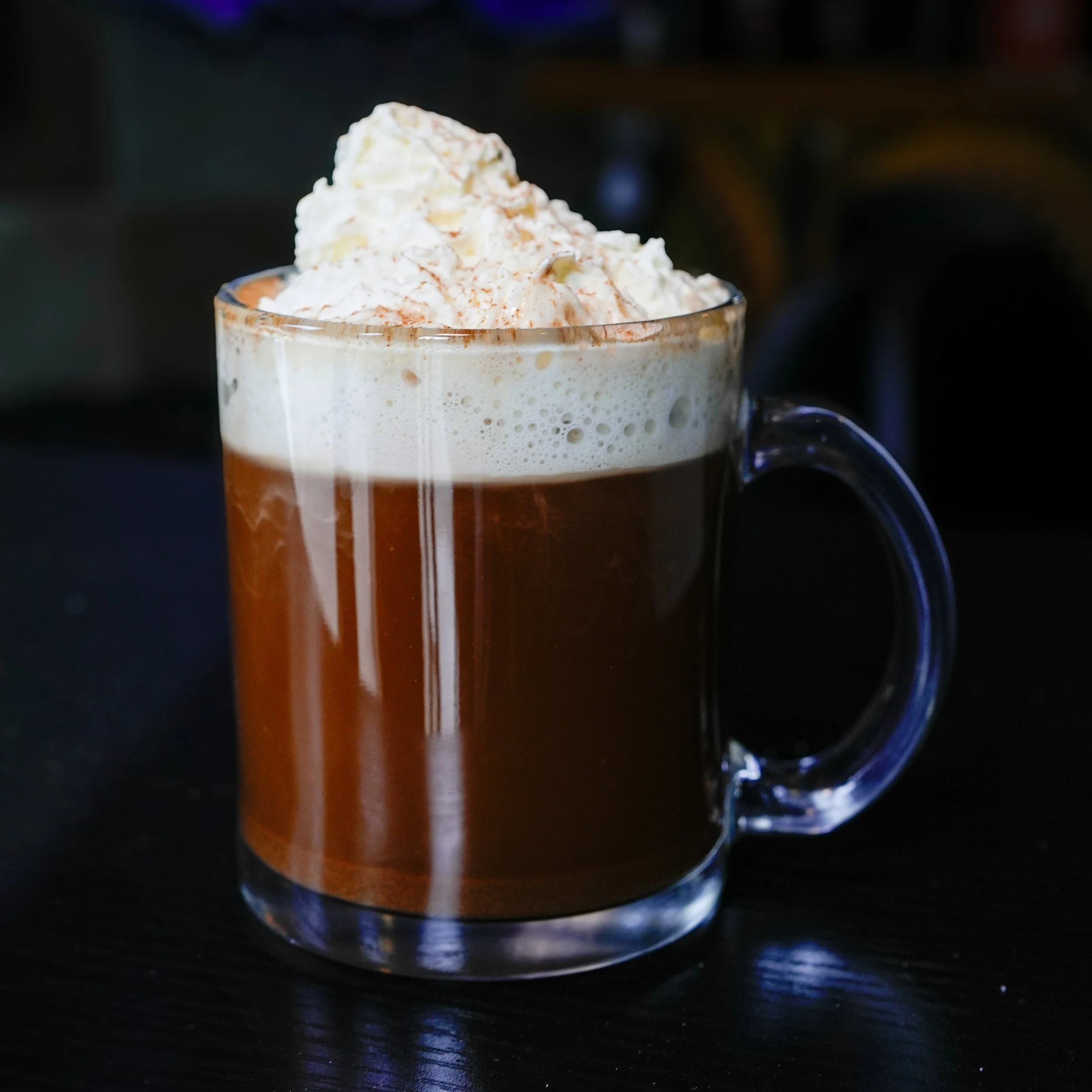 Muse Mushroom Coffee topped with whipped cream and cinnamon in a clear glass mug.