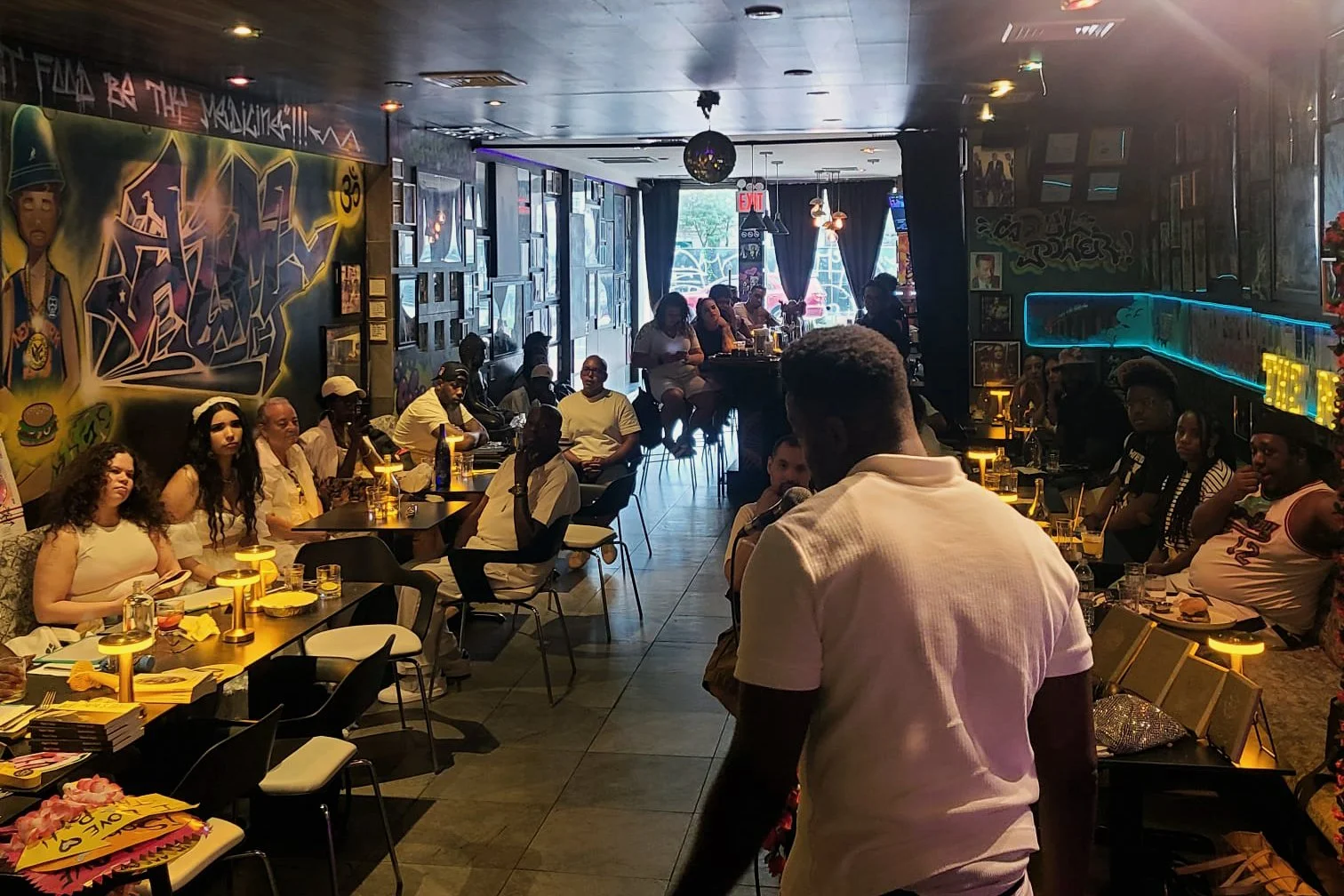 Guests enjoying an event at Urban Vegan Kitchen in Chelsea, with colorful artwork and the illuminated bar in view.