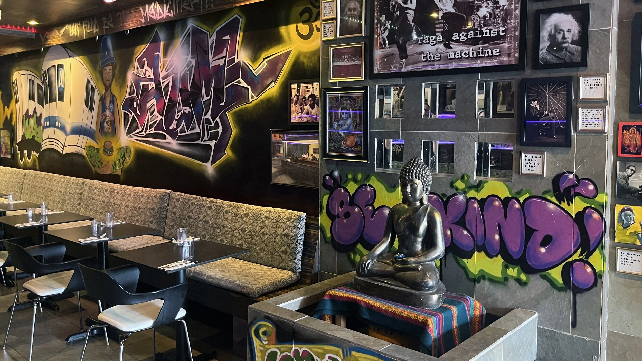 Interior of Urban Vegan Kitchen featuring graffiti murals, New York subway artwork, a Buddha statue, and walls celebrating music, art, and culture.