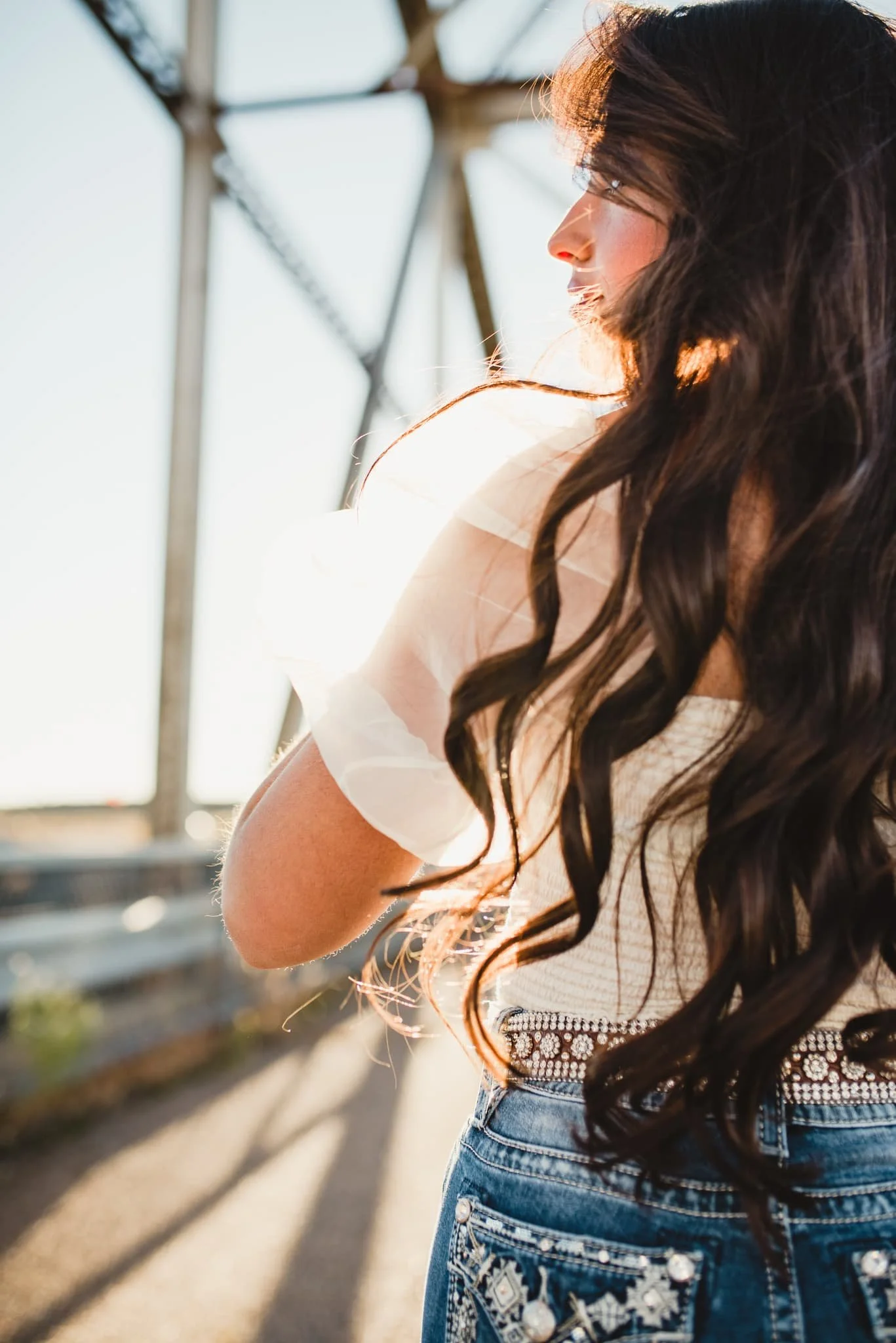 Girl in white blouse from behind, her side profile and long hair is featured