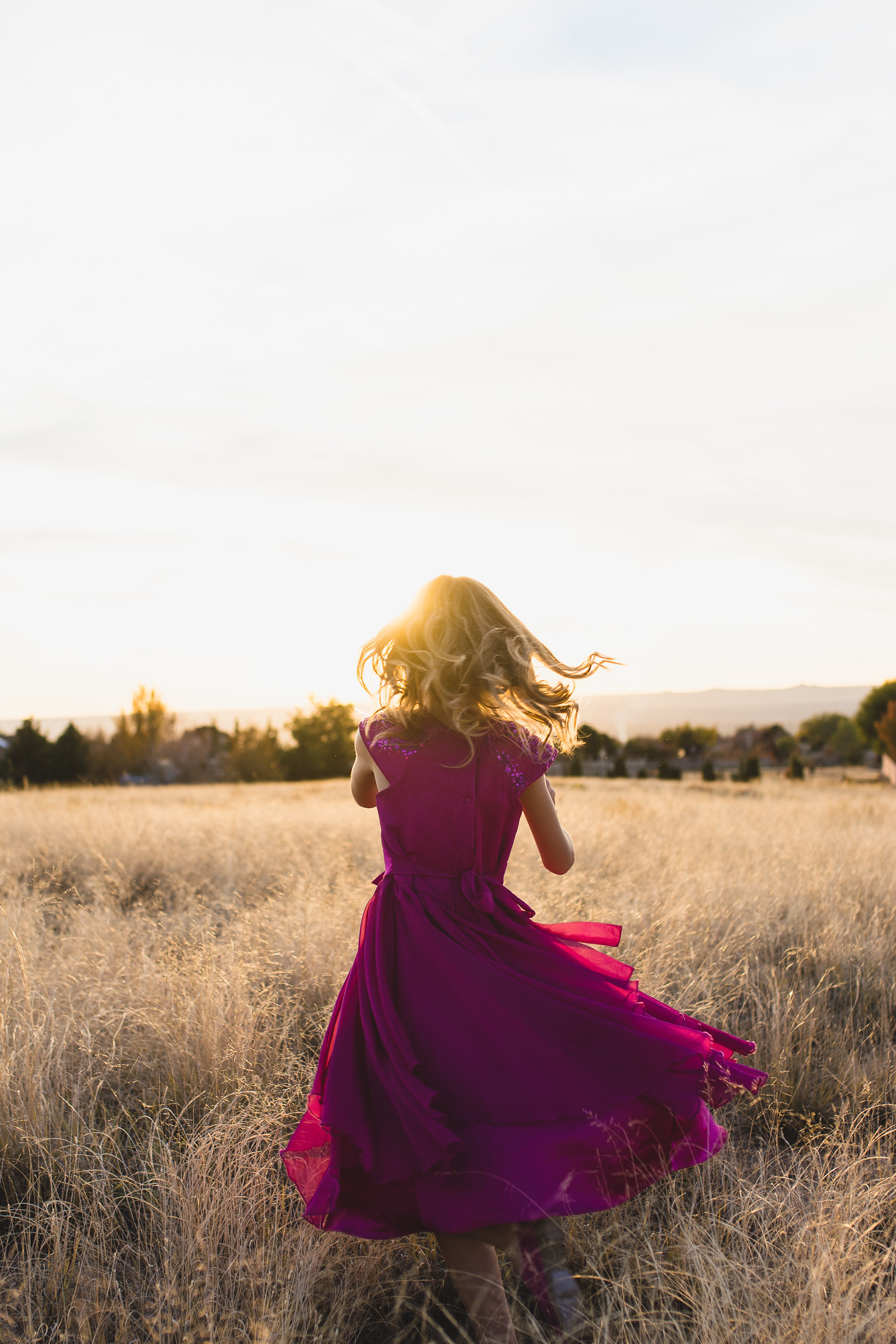 Girl twirling in pink dress in yellow sun-drenched field in Albuquerque