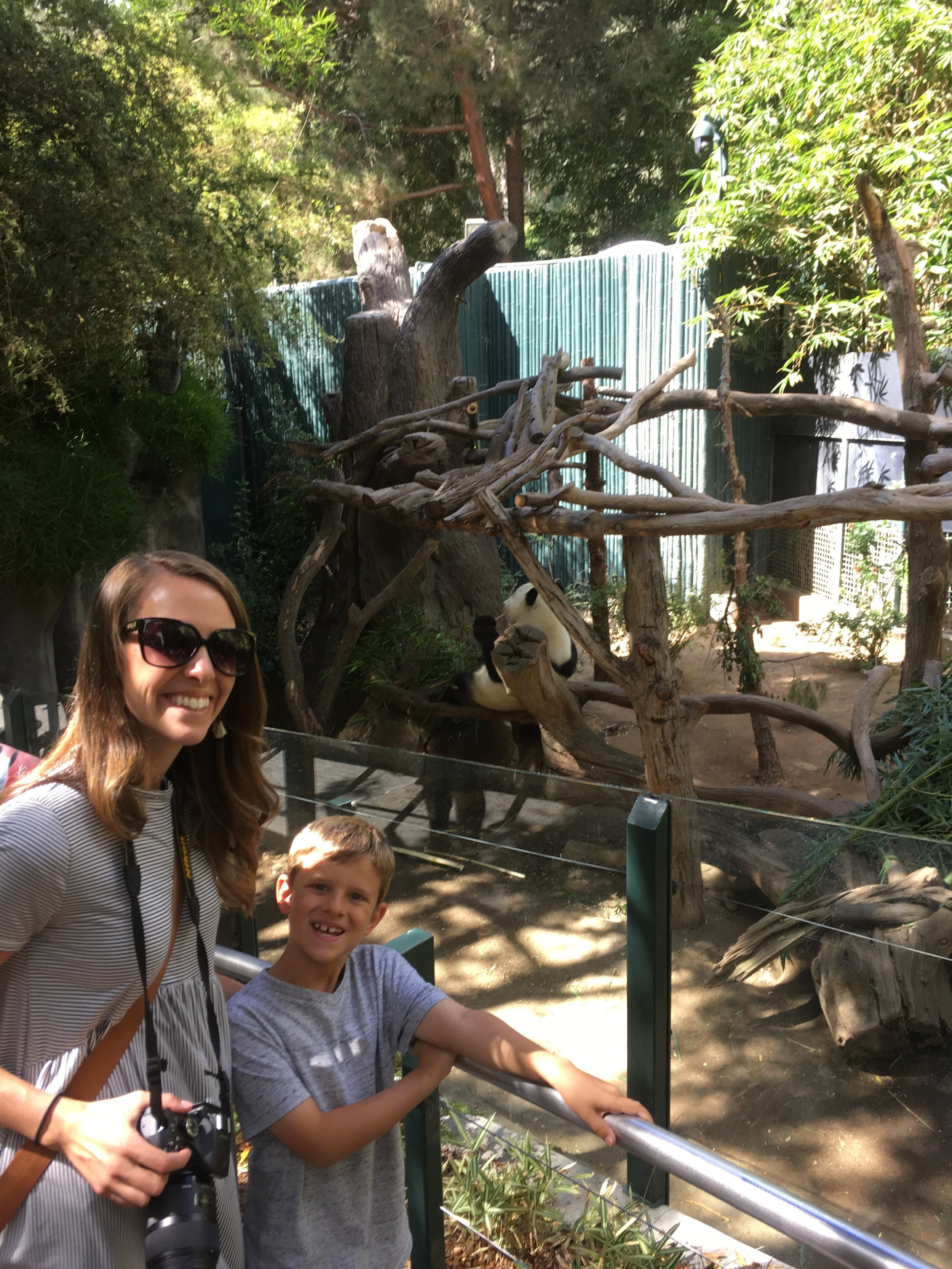 Mom and son posing with panda in background at zoo