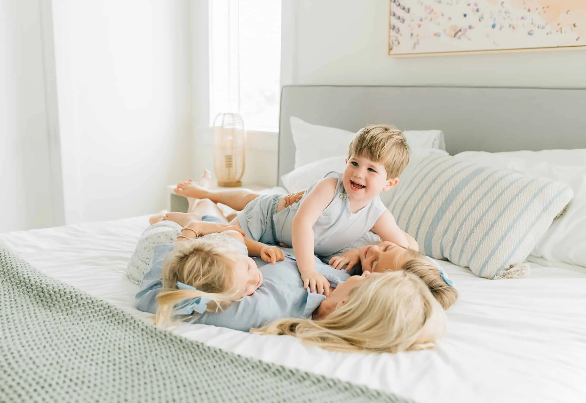 mom laying down on bed while her three young kids lay on her and laugh