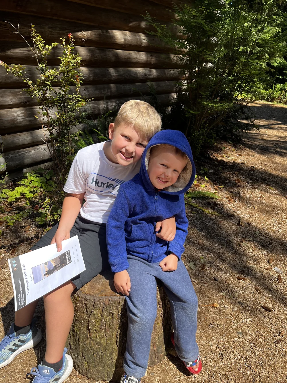 Two boys smiling while sitting on tree stump