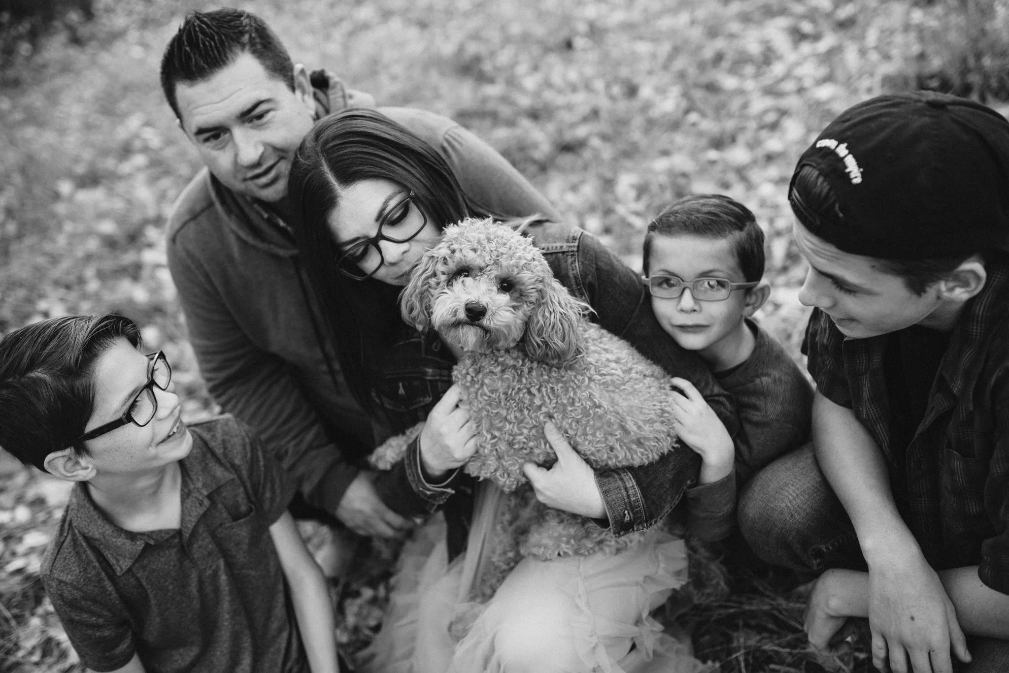 Black and white image of family kneeling and hugging their dog