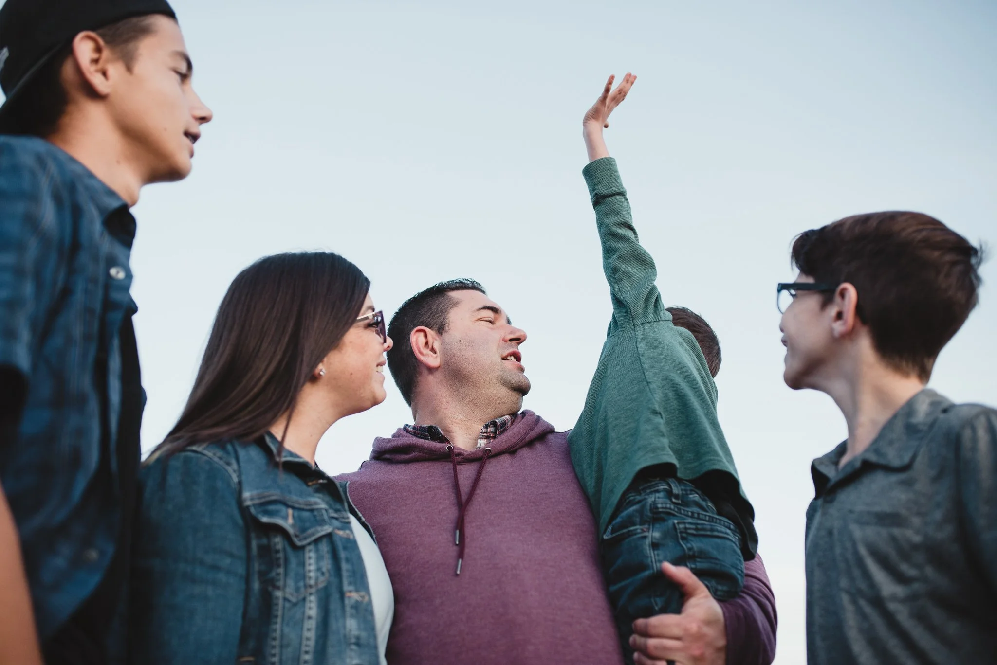 From below of family with three boys standing close together as youngest boy reaches for the sky