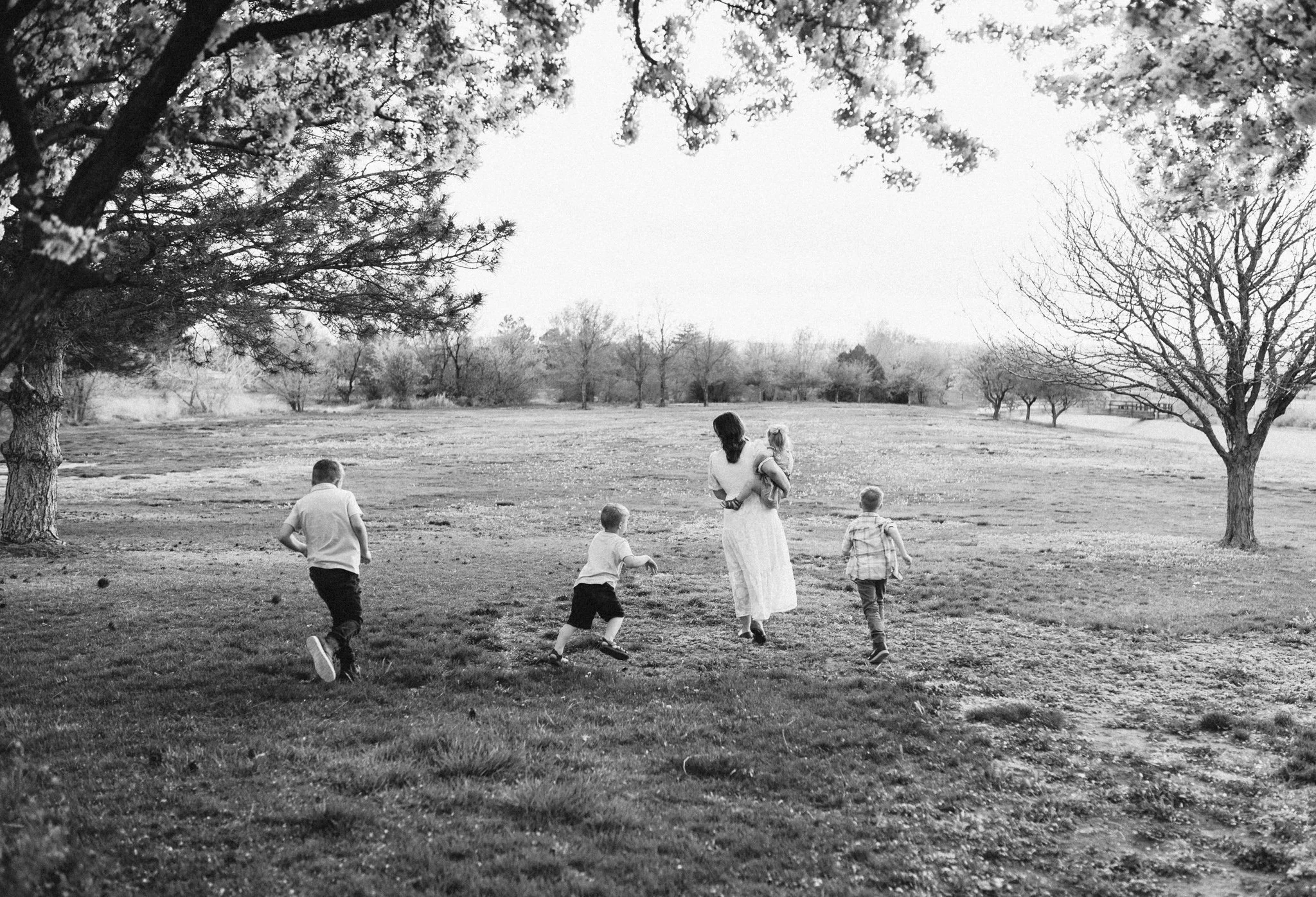 Mom holding baby and walking with her three other kids in a field with trees