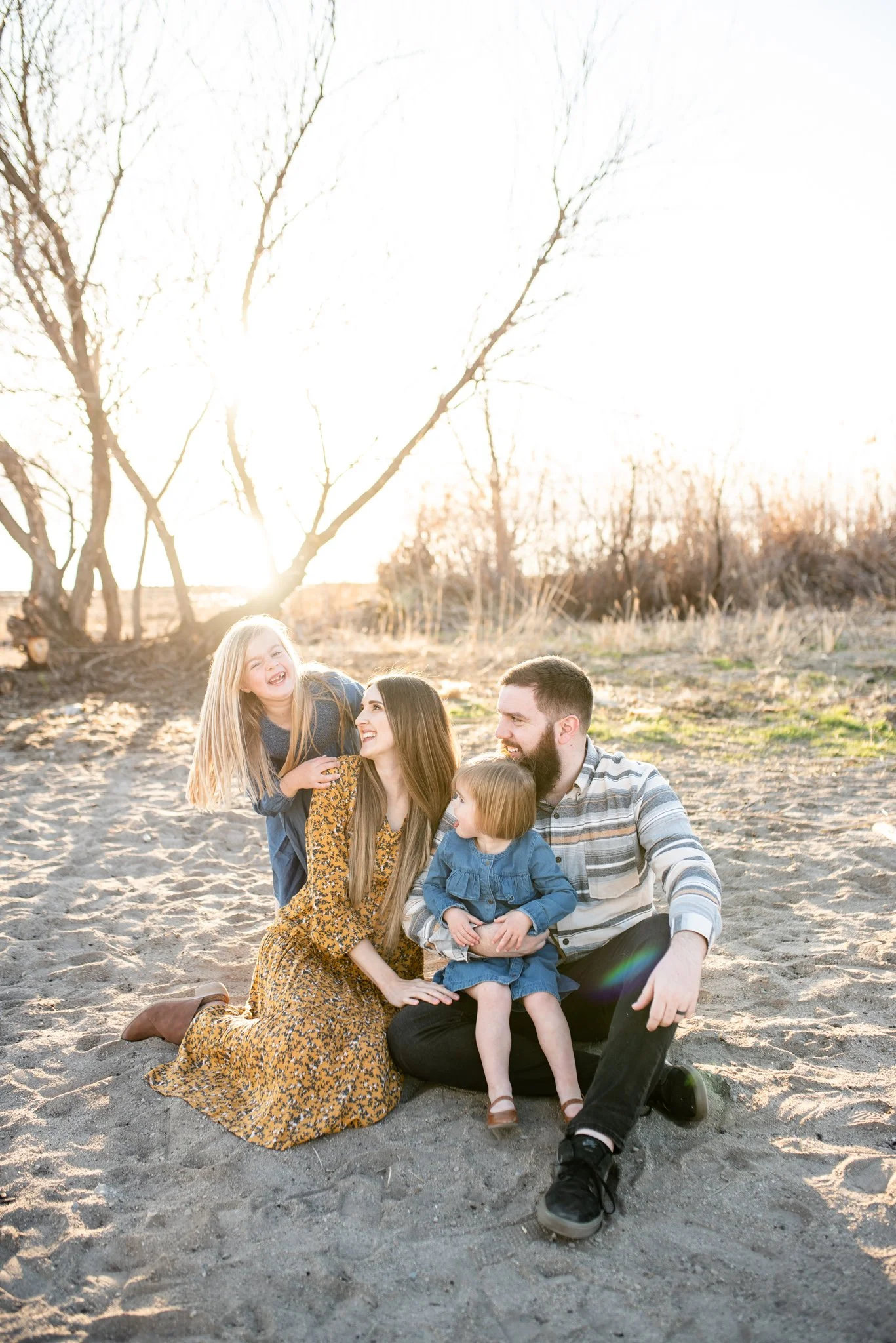 Mom and dad with one daughter in dad's lap while the other laughs behind mom's shoulder