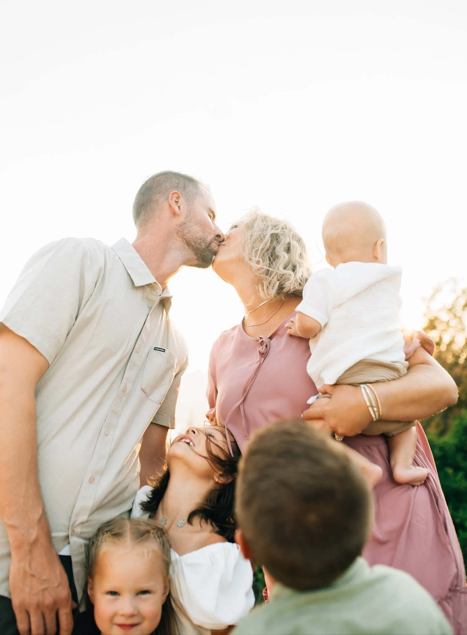 Parents lean over to kiss while three kids watch