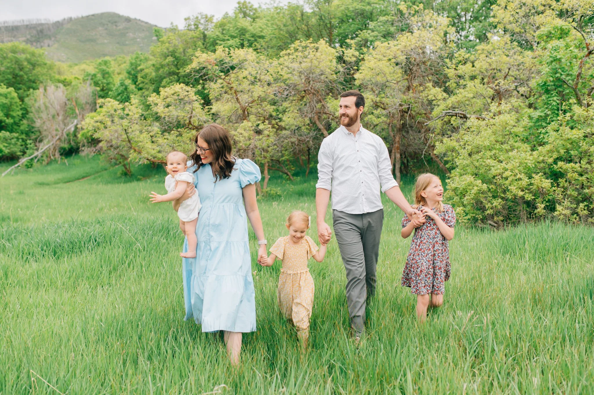 Family with three young daughters walking through green field with tall grass