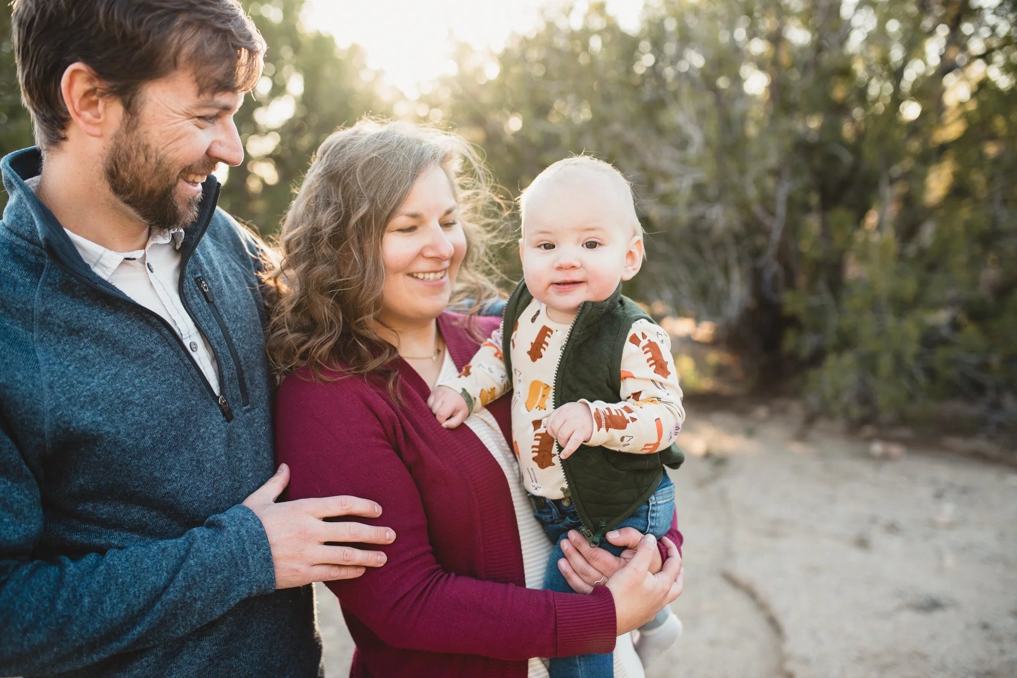 Mom holds baby, dad is behind mom, baby looks at camera