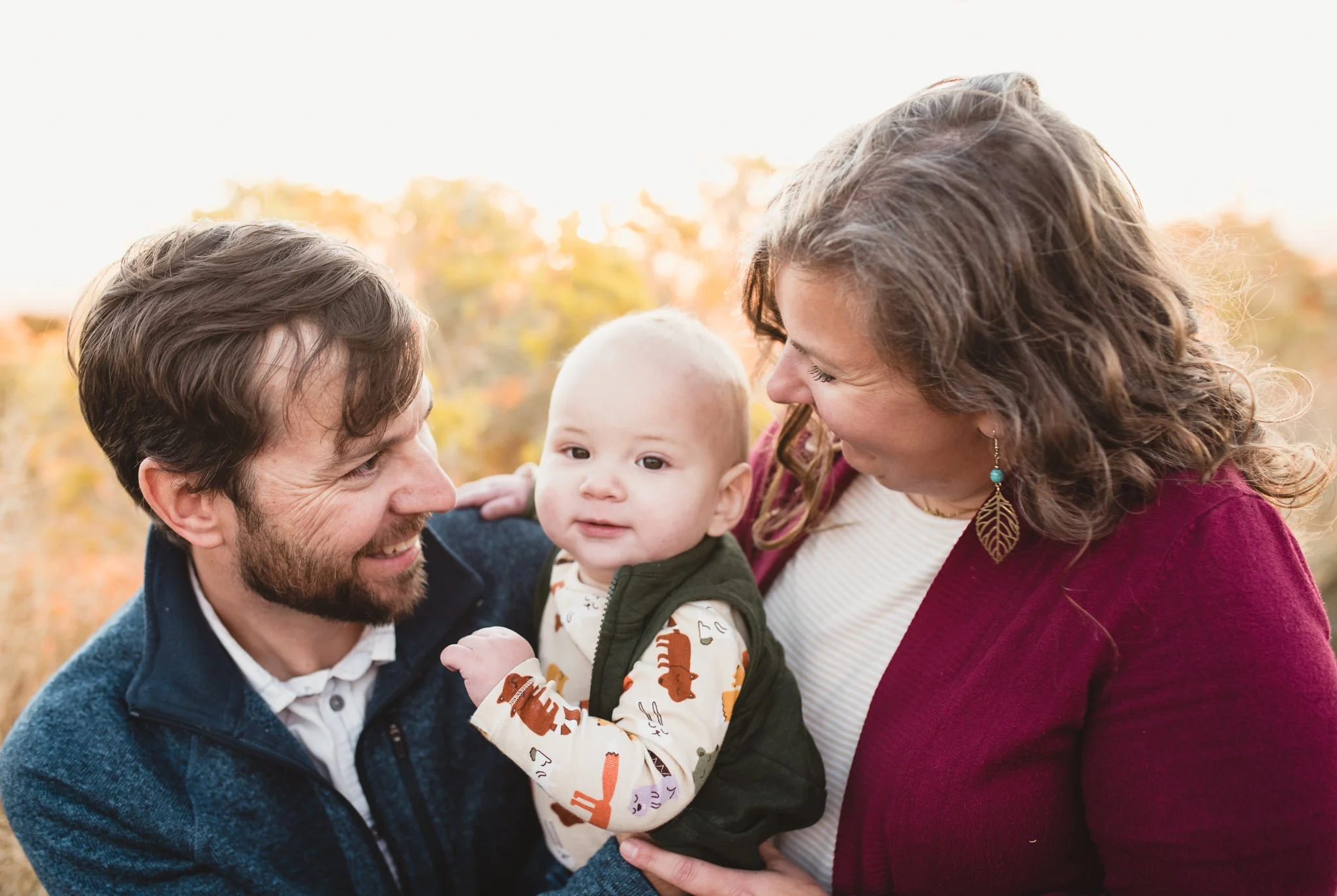 Baby being held by both parents as they look and smile at him