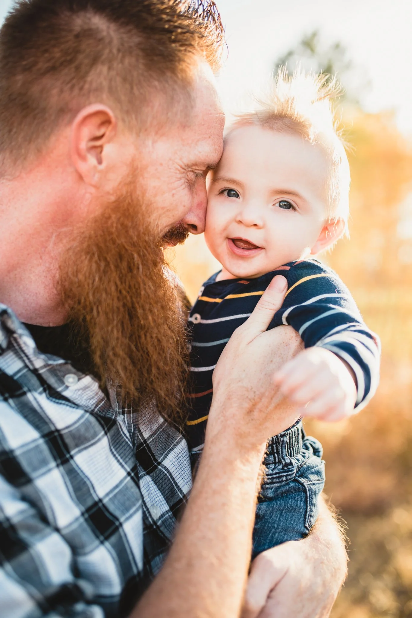 Dad puts forehead against baby's cheek as he smiles at the camera