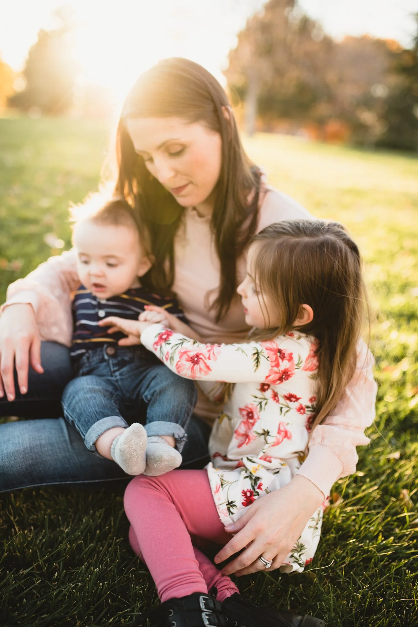 Mom sitting in green grass as she holds both her kids