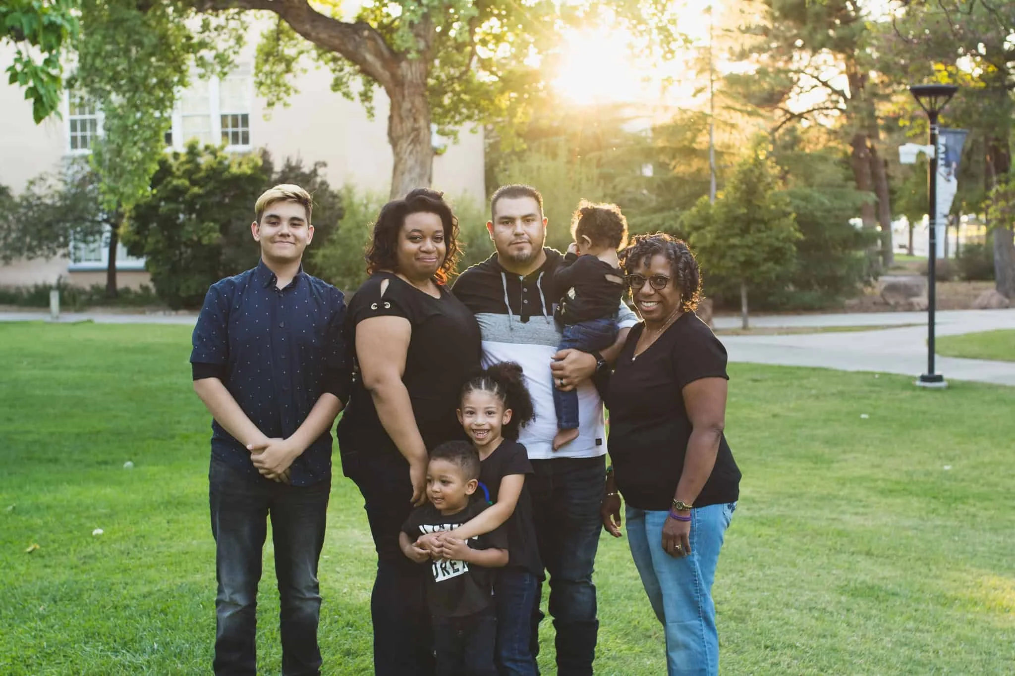 Family with four kids and grandma standing together and smiling in green grass on college campus