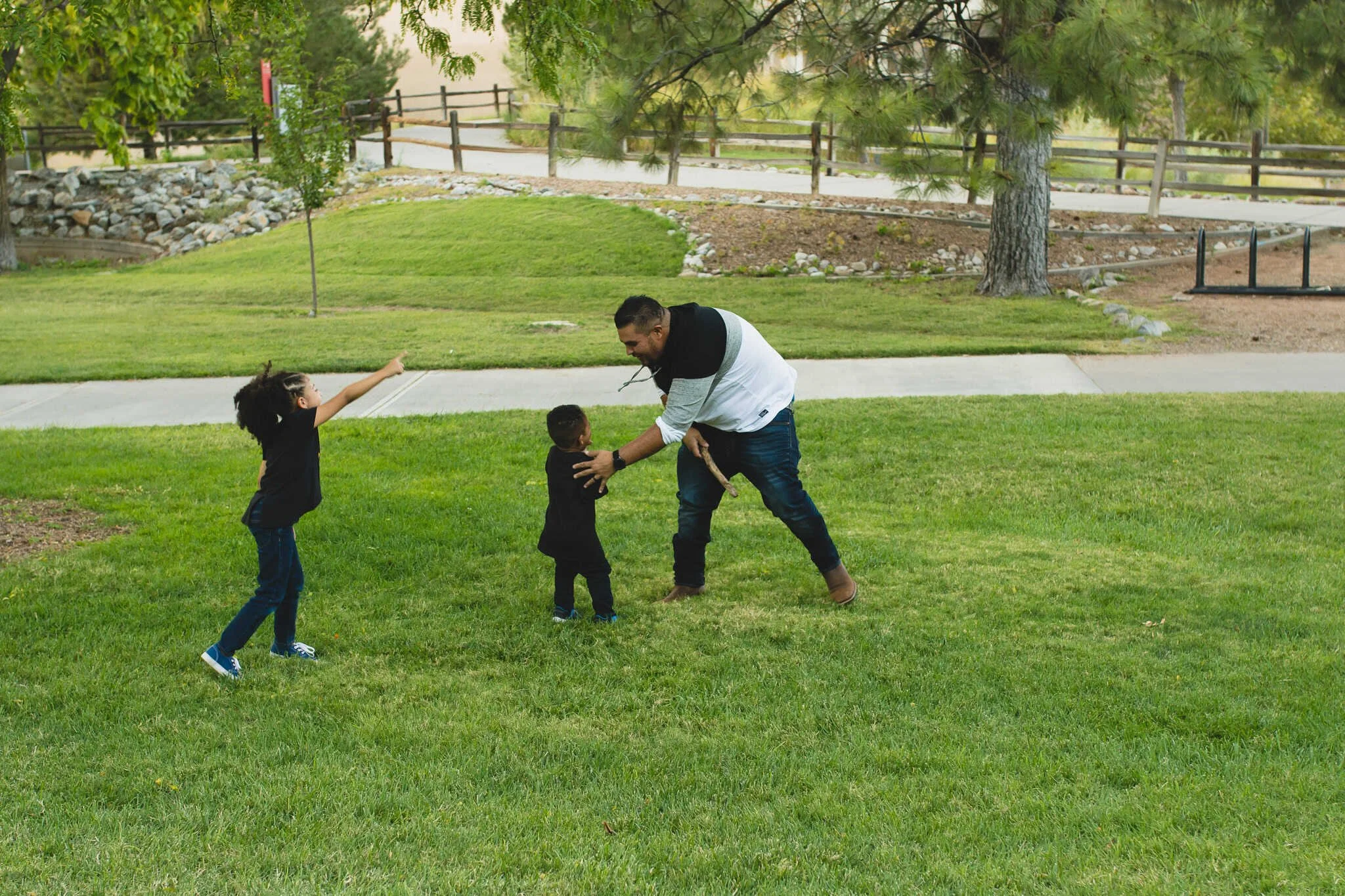 Dad running around and chasing two kids in green grass