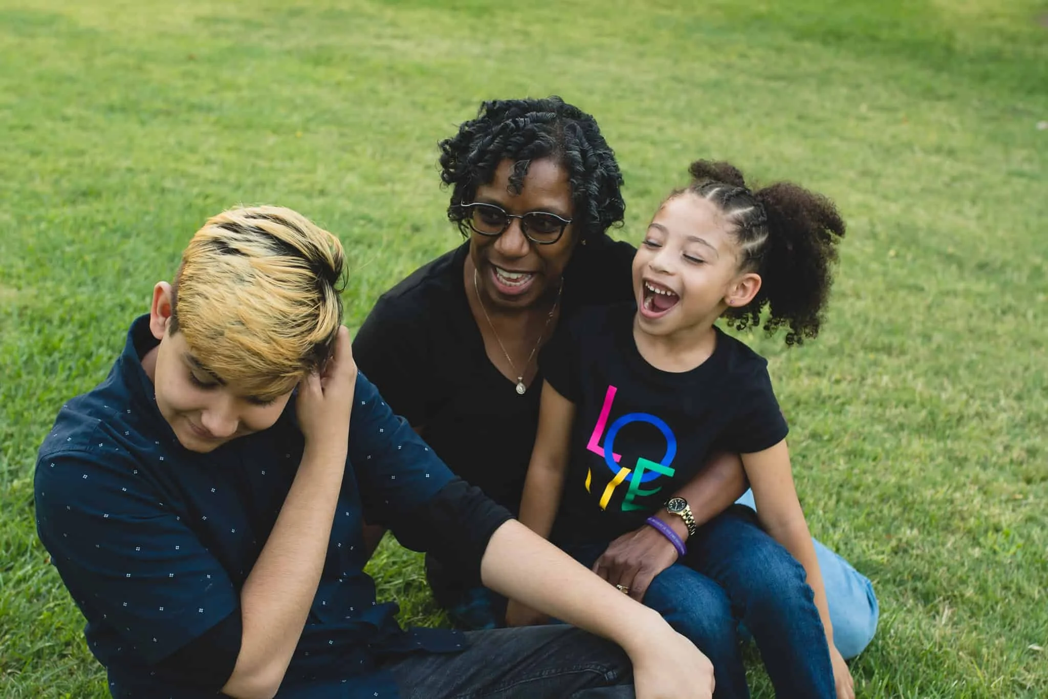 Grandma sitting in grass with teenage grandson and little granddaughter