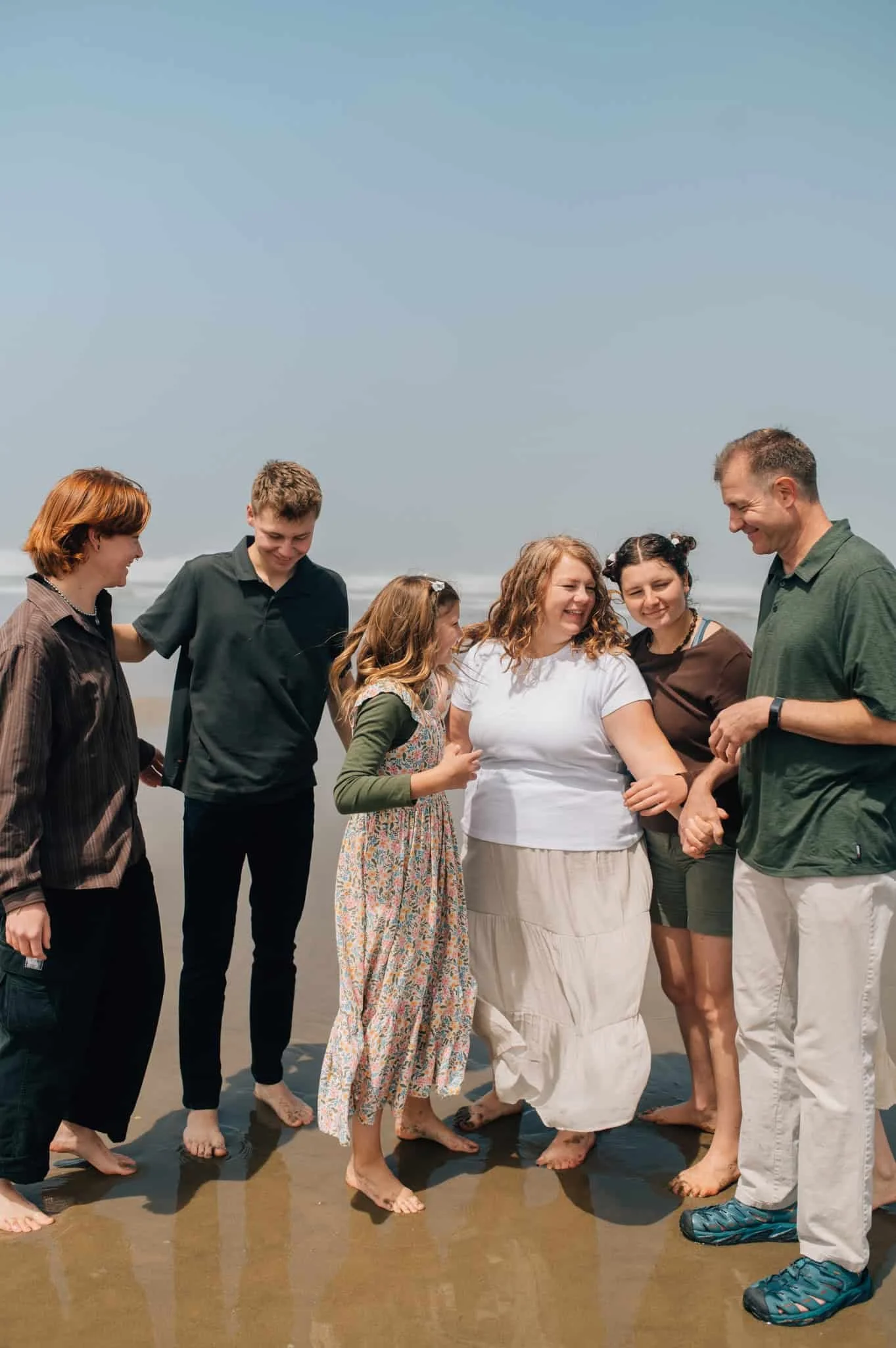 Family hugs and laughs on shore with ocean behind them at Canon Beach
