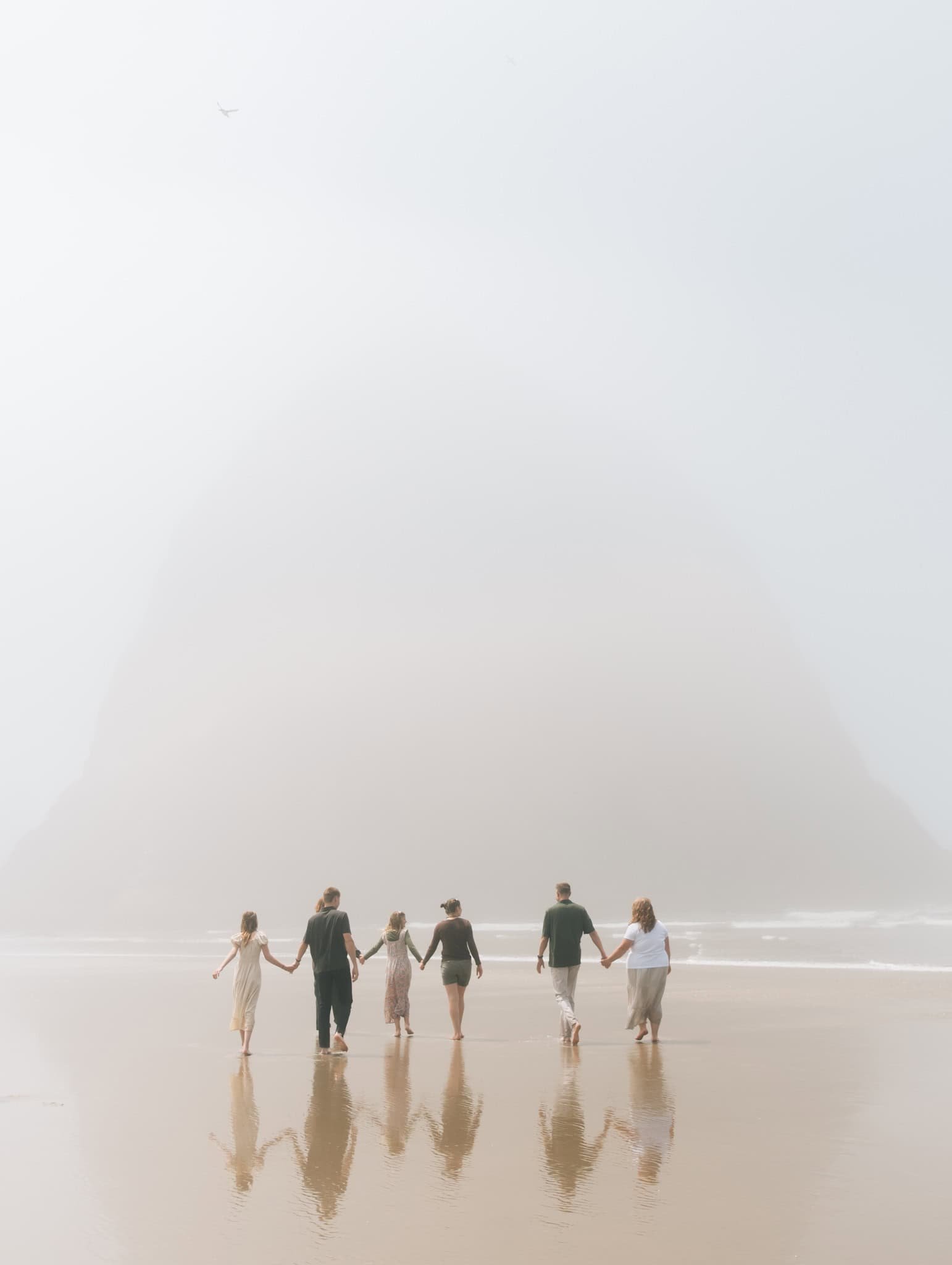 Family with older kids holding hands and walking towards giant rock at Cannon Beach, OR