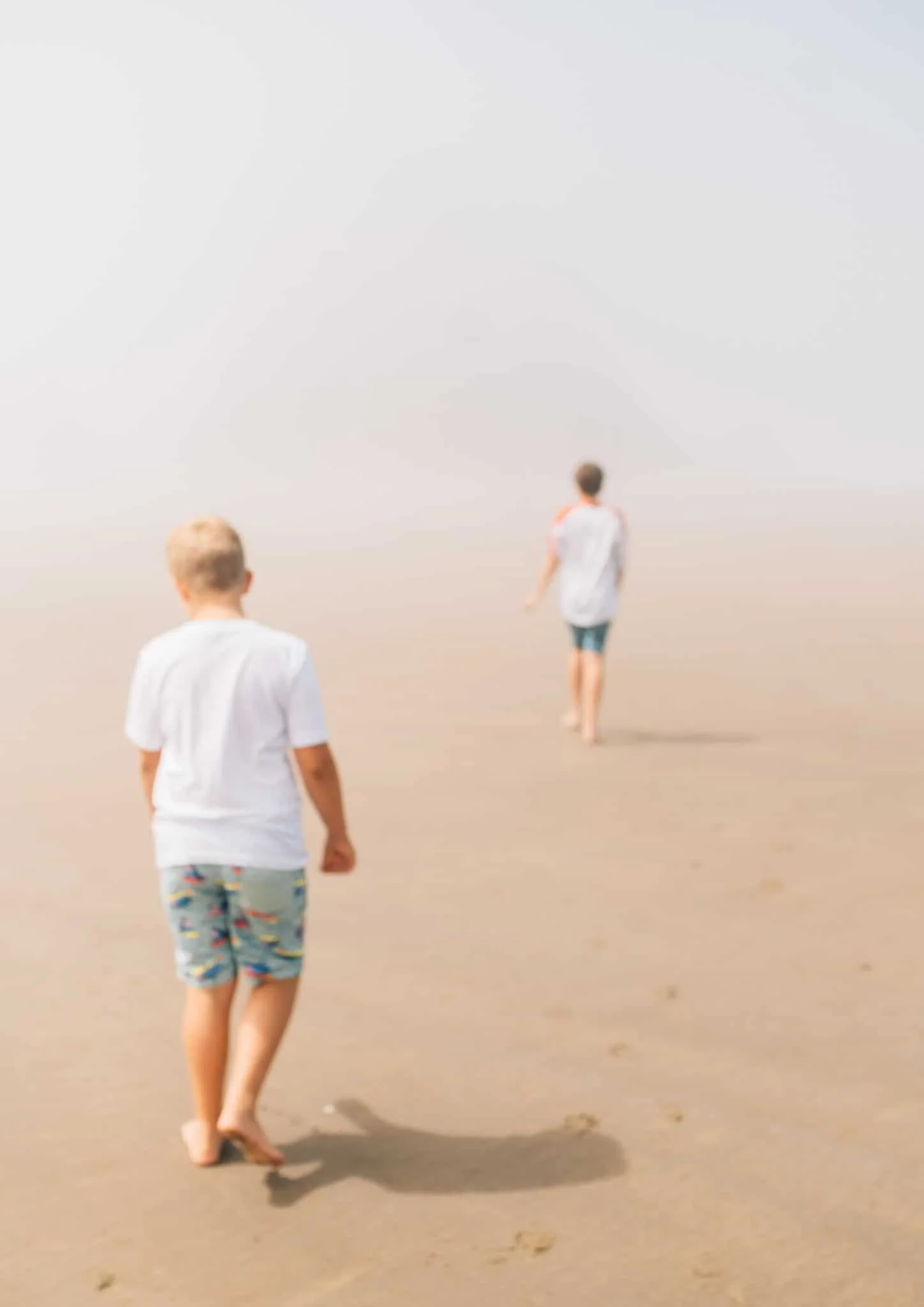 Two boys walking on the foggy shore towards ocean at Cannon Beach