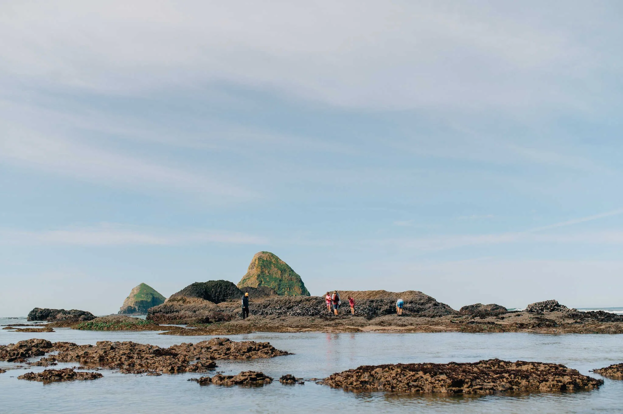 Far away image of people on rock formations in ocean at Tunnel Beach