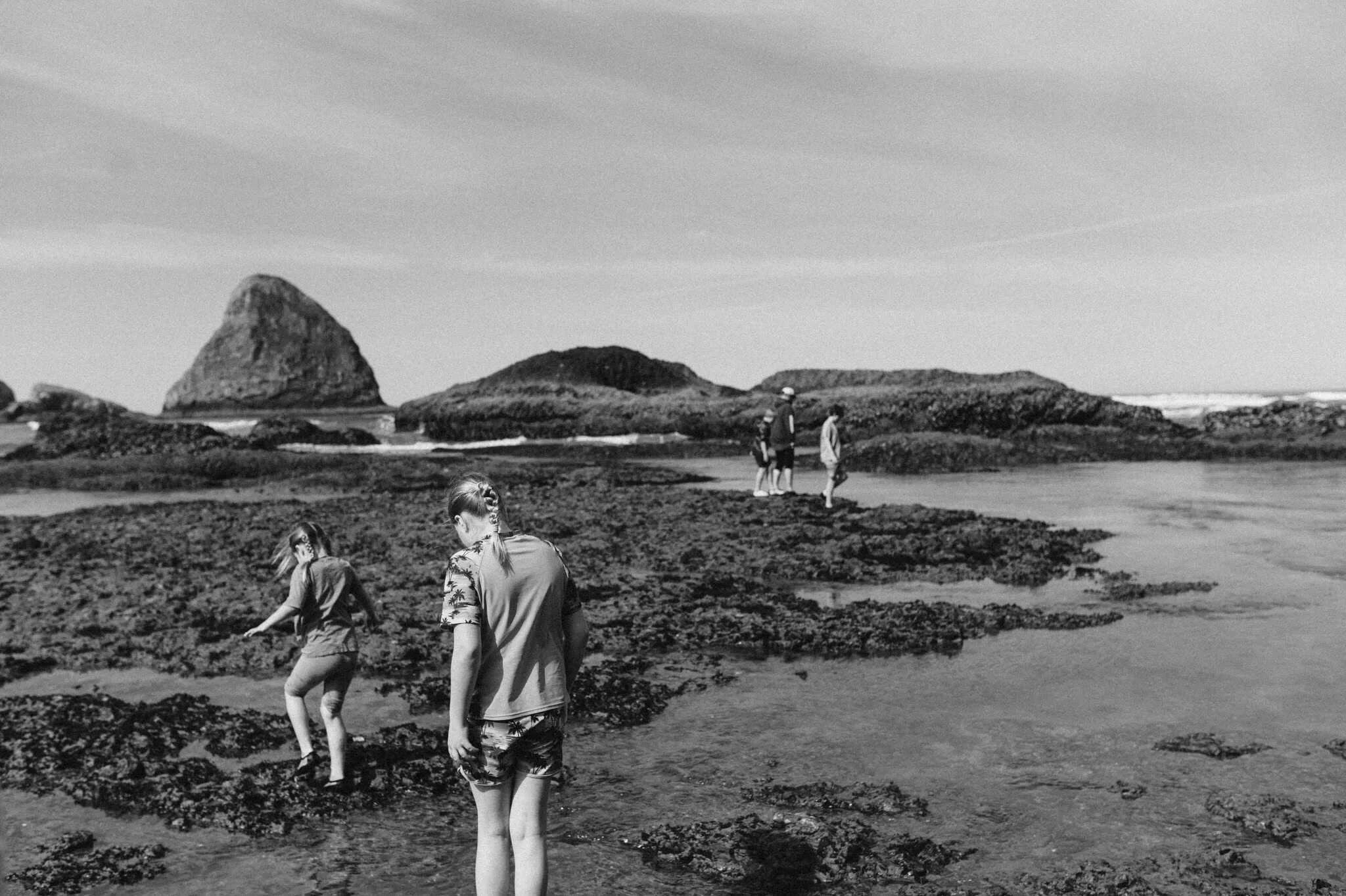 Black and white image of two girls headings towards group along rock formations at Tunnel beach