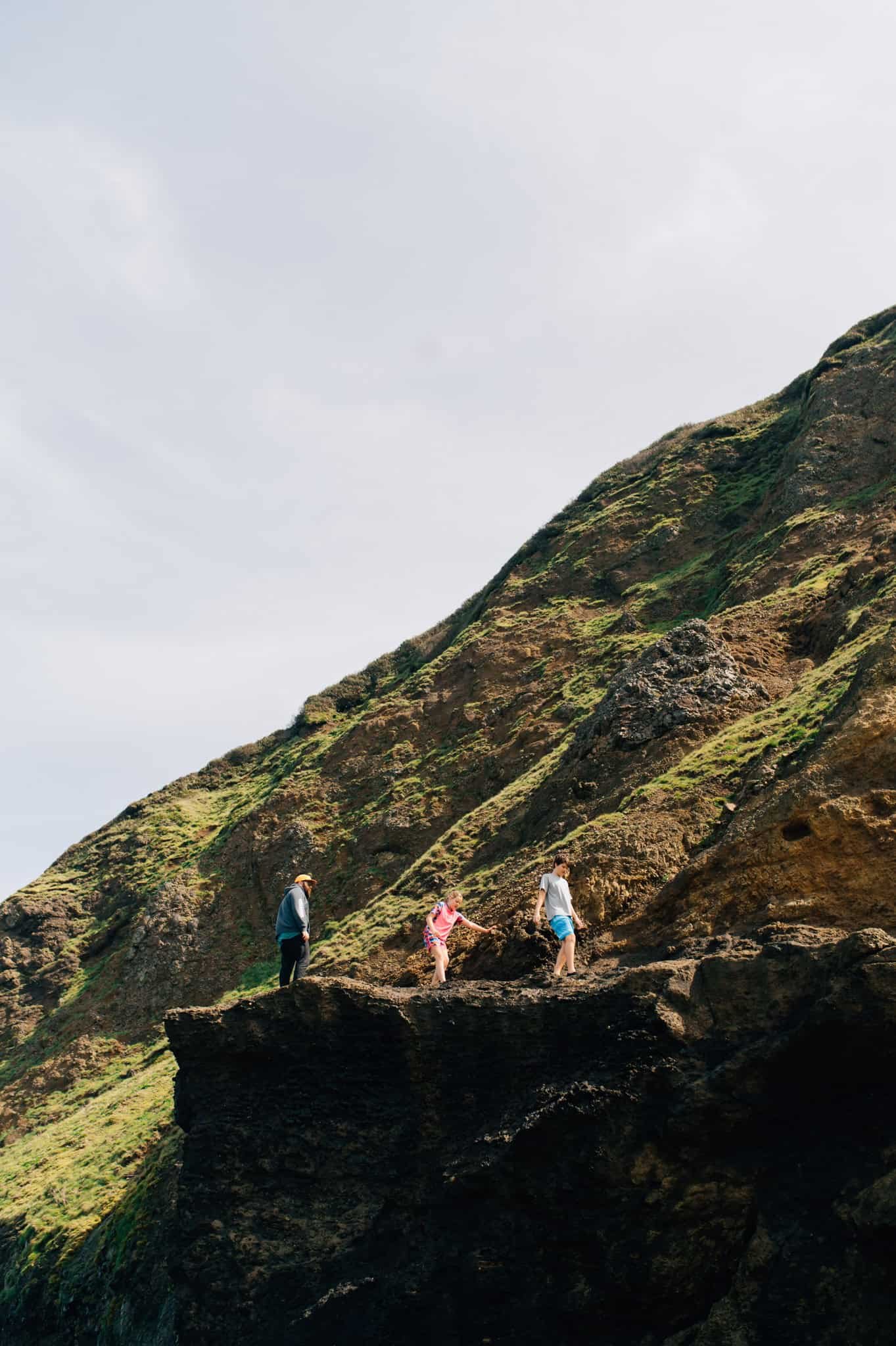 A man and two older kids on a rocky ledge with green hills behind them along Oregon coast