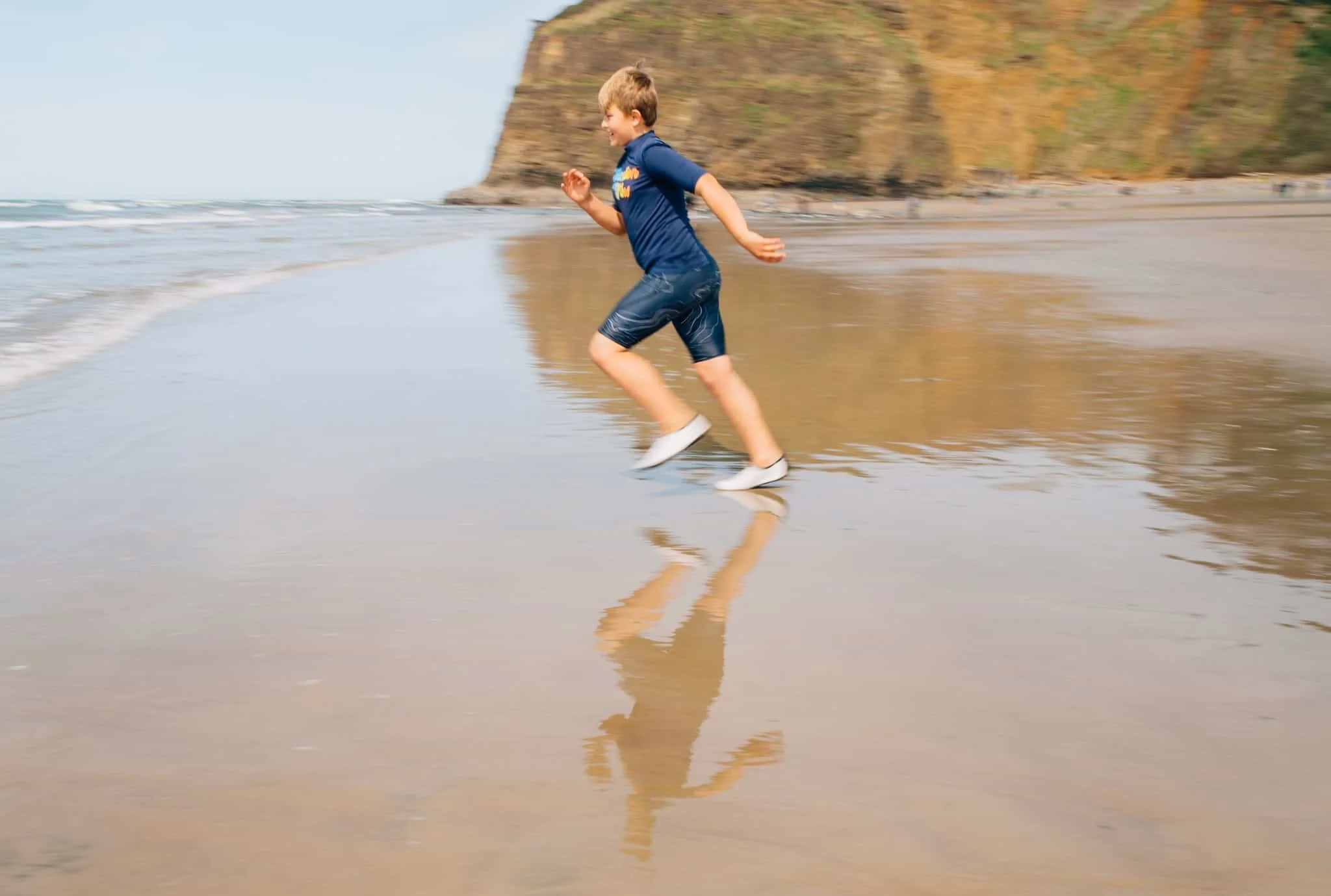 a boy running into the ocean at Tunnel Beach