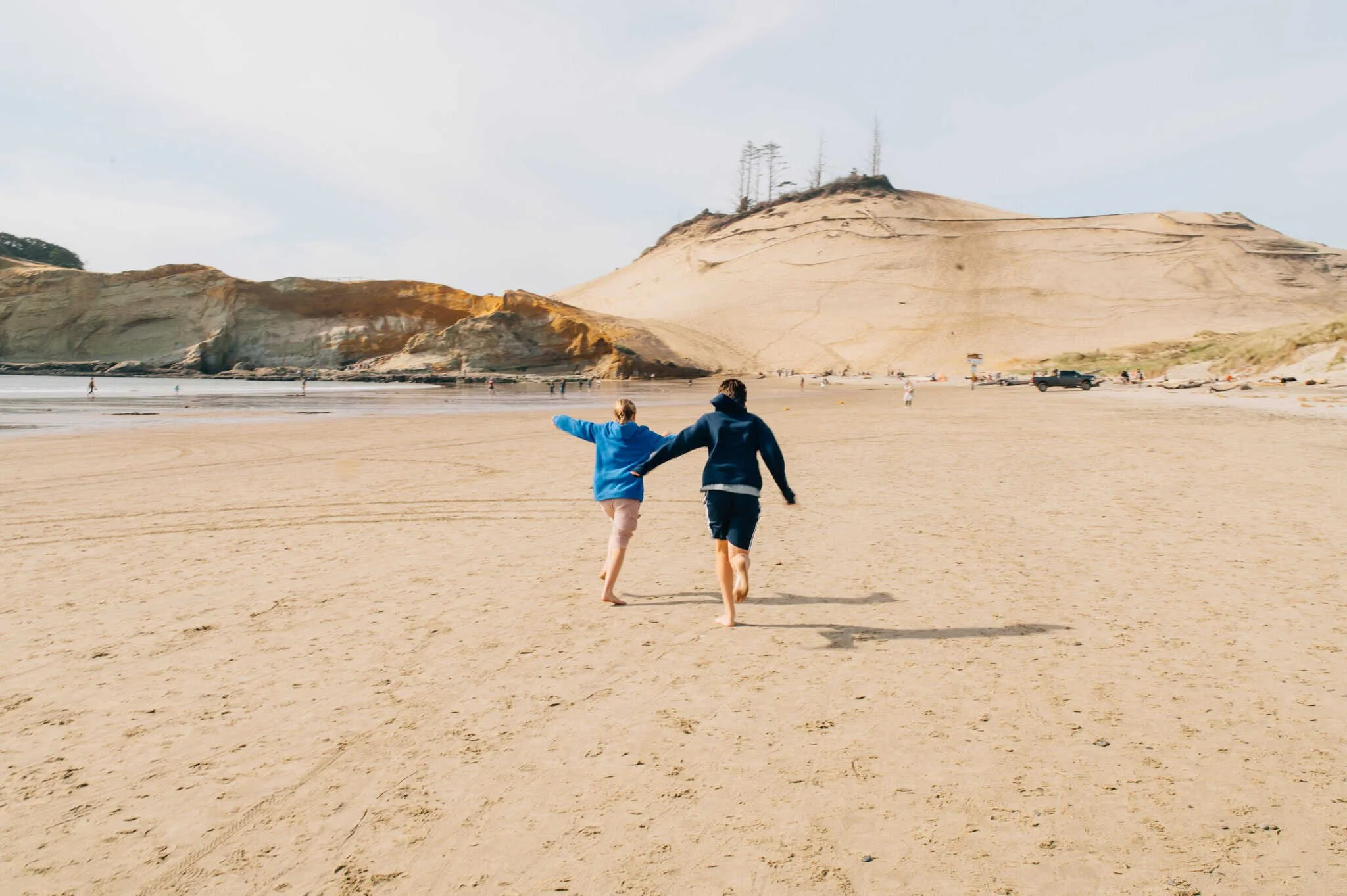 Two teenagers run towards Cape Kiwanda, OR