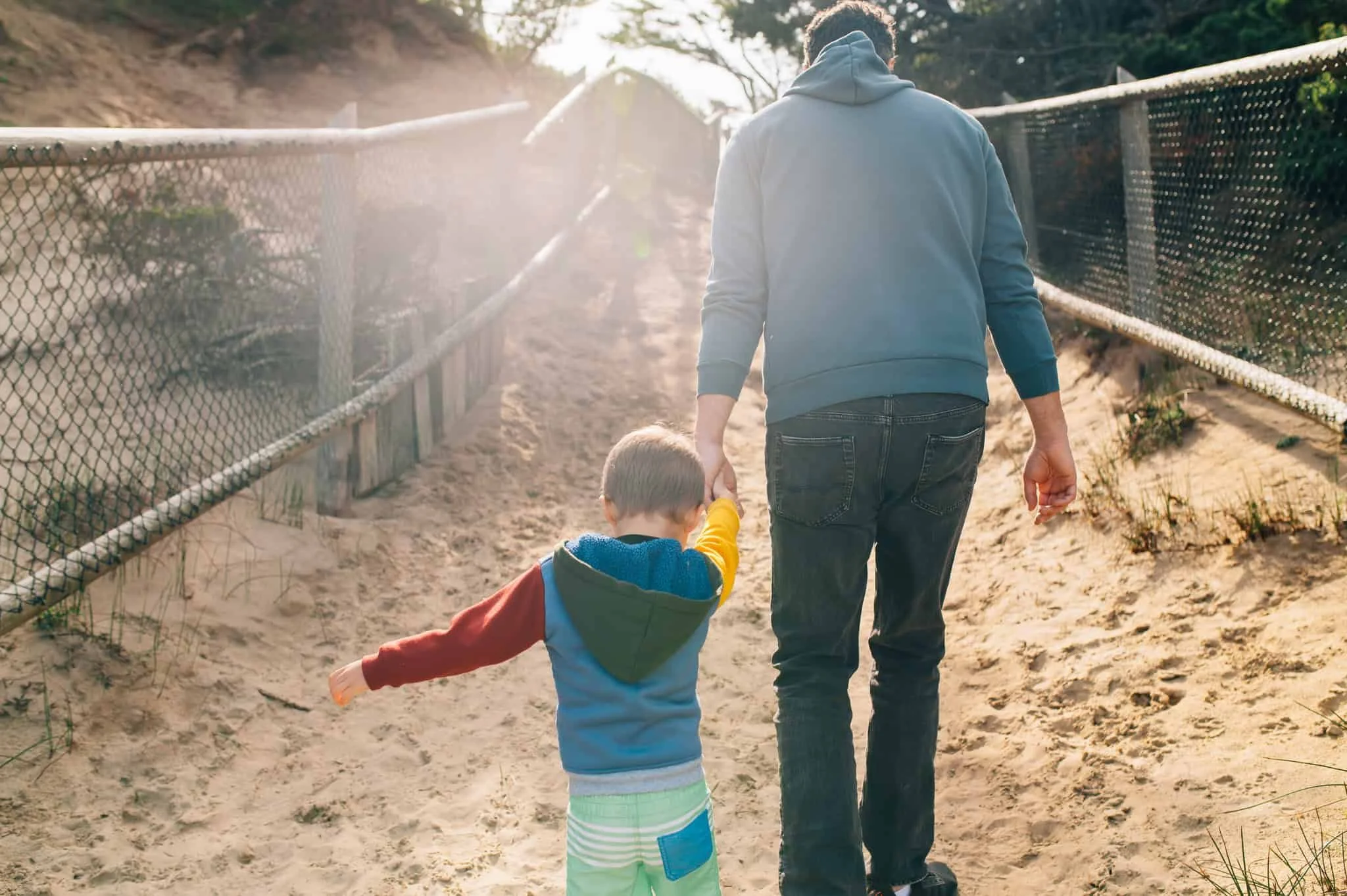 A man holds the hand of his son while they walk a sandy path on Cape Kiwanis