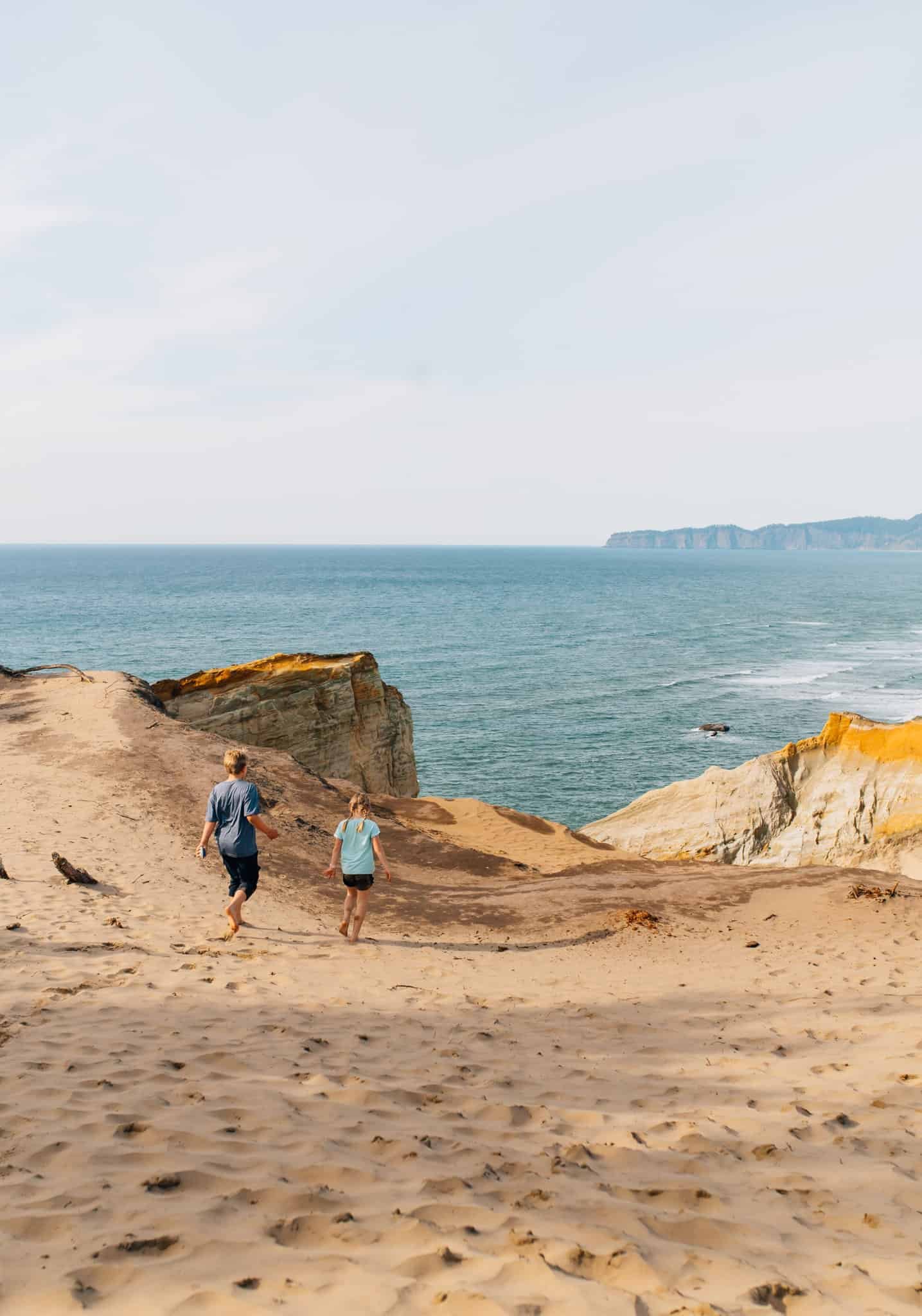A boy and girl walking on top of a sand dune with ocean in the distance at Cape Kiwanis