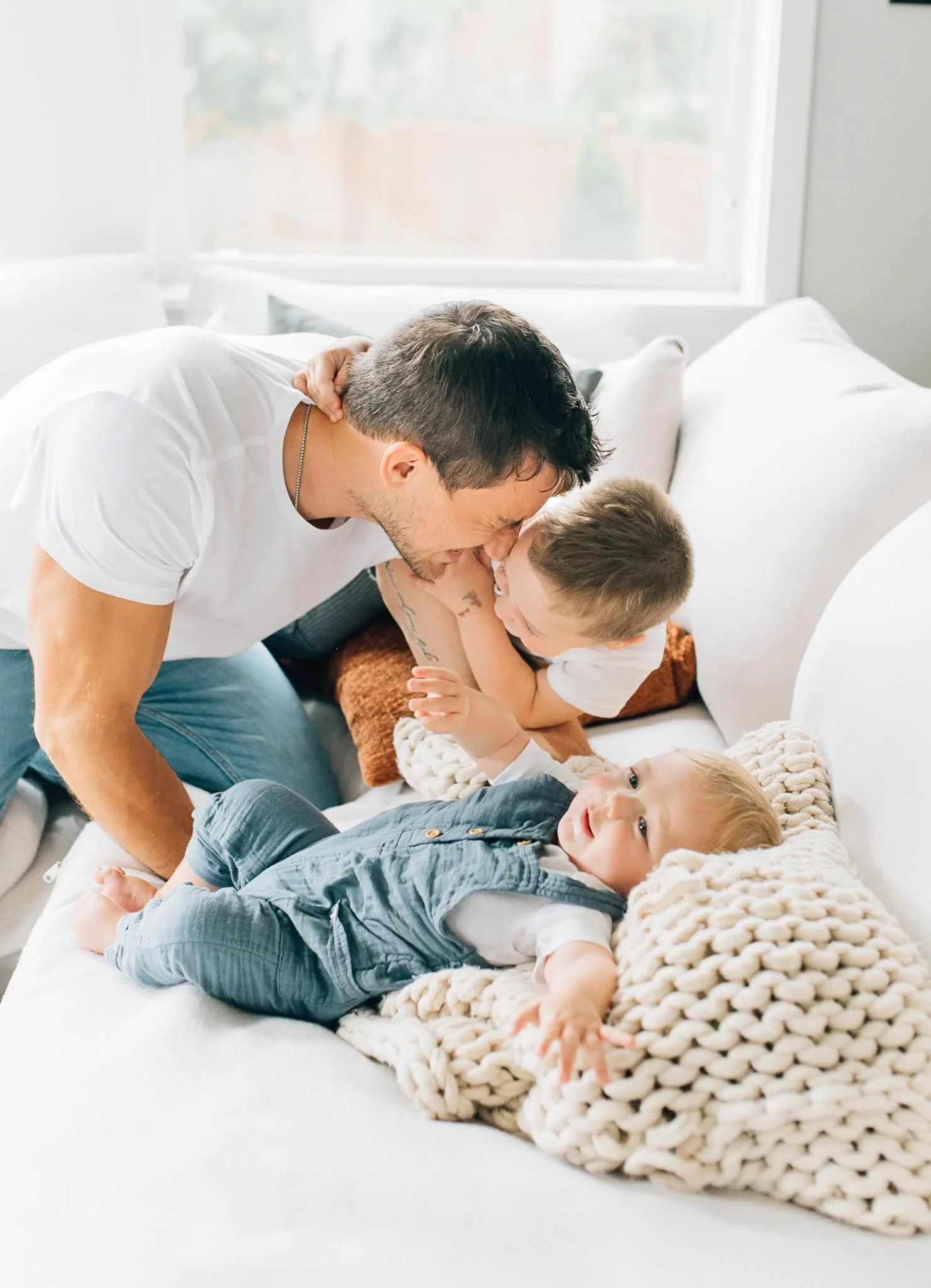 dad leans down to wrestle two little boys on the couch