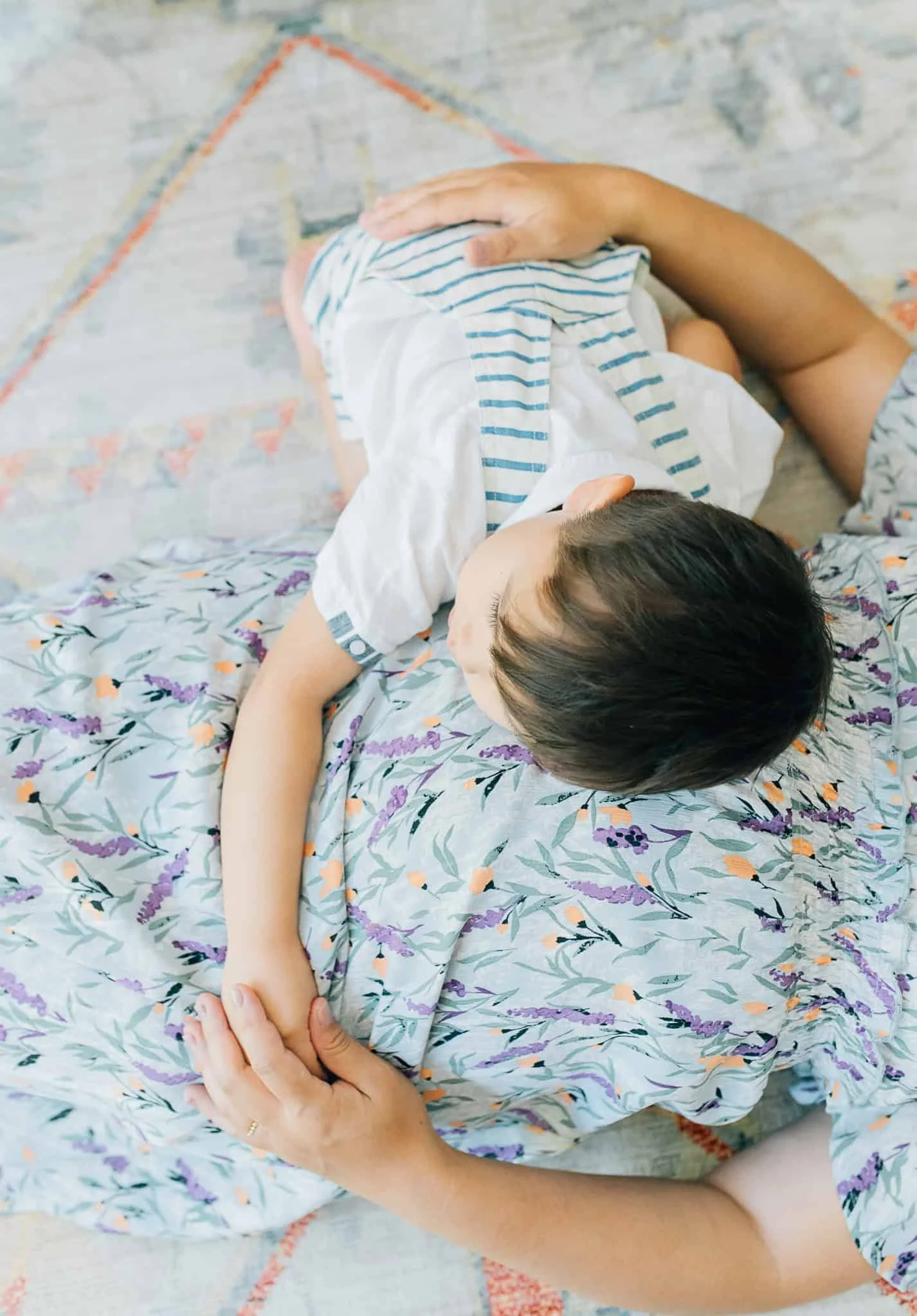 little boy lays on mom's stomach and holds her hand