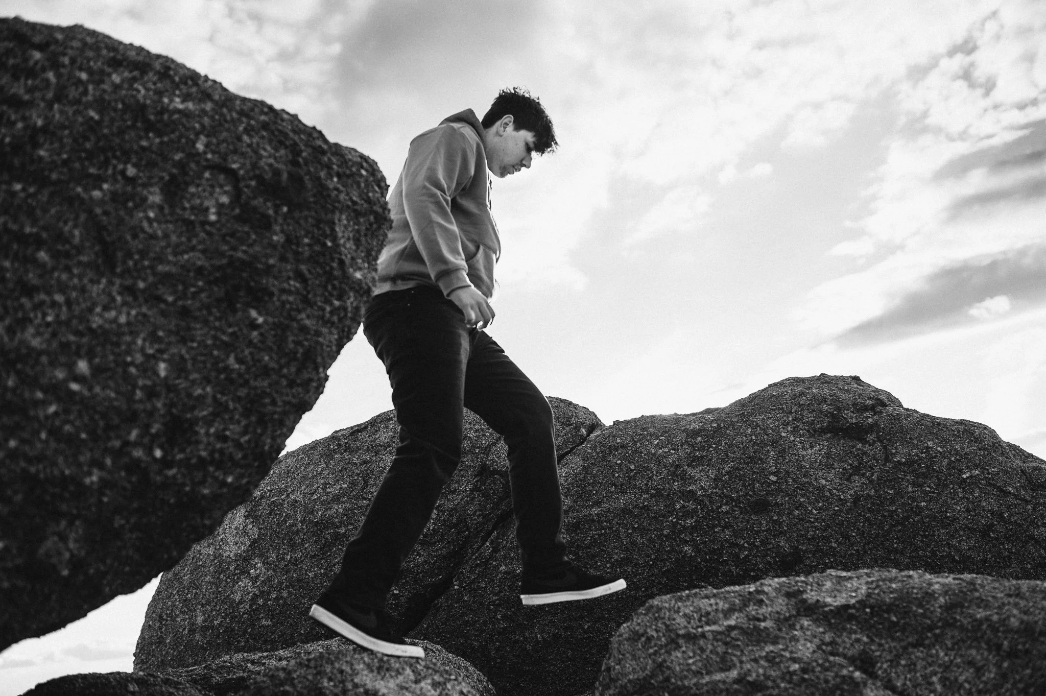 Senior boy in black jeans and hoodie climbs rocks