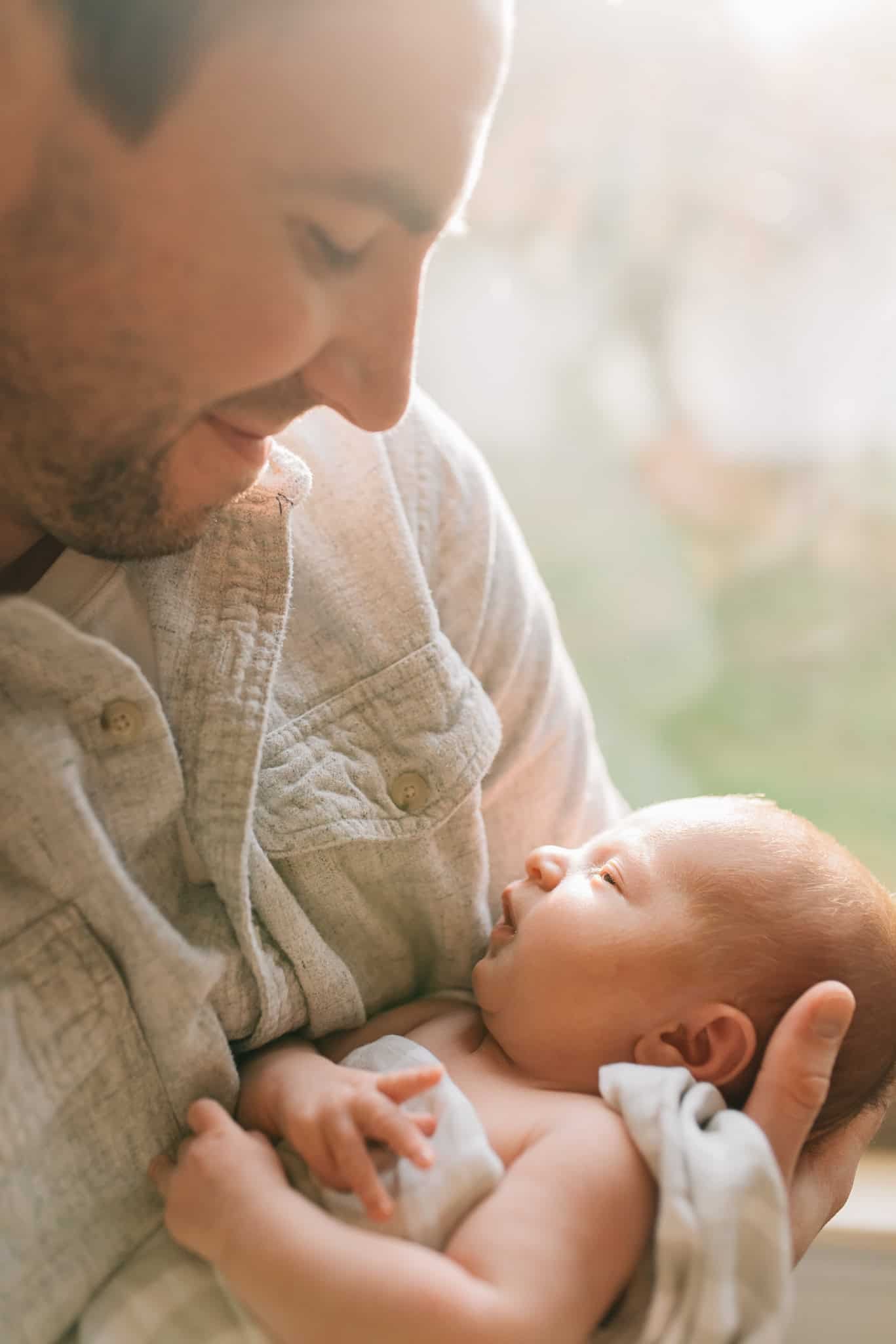 dad looks down at newborn baby with hazy light behind him